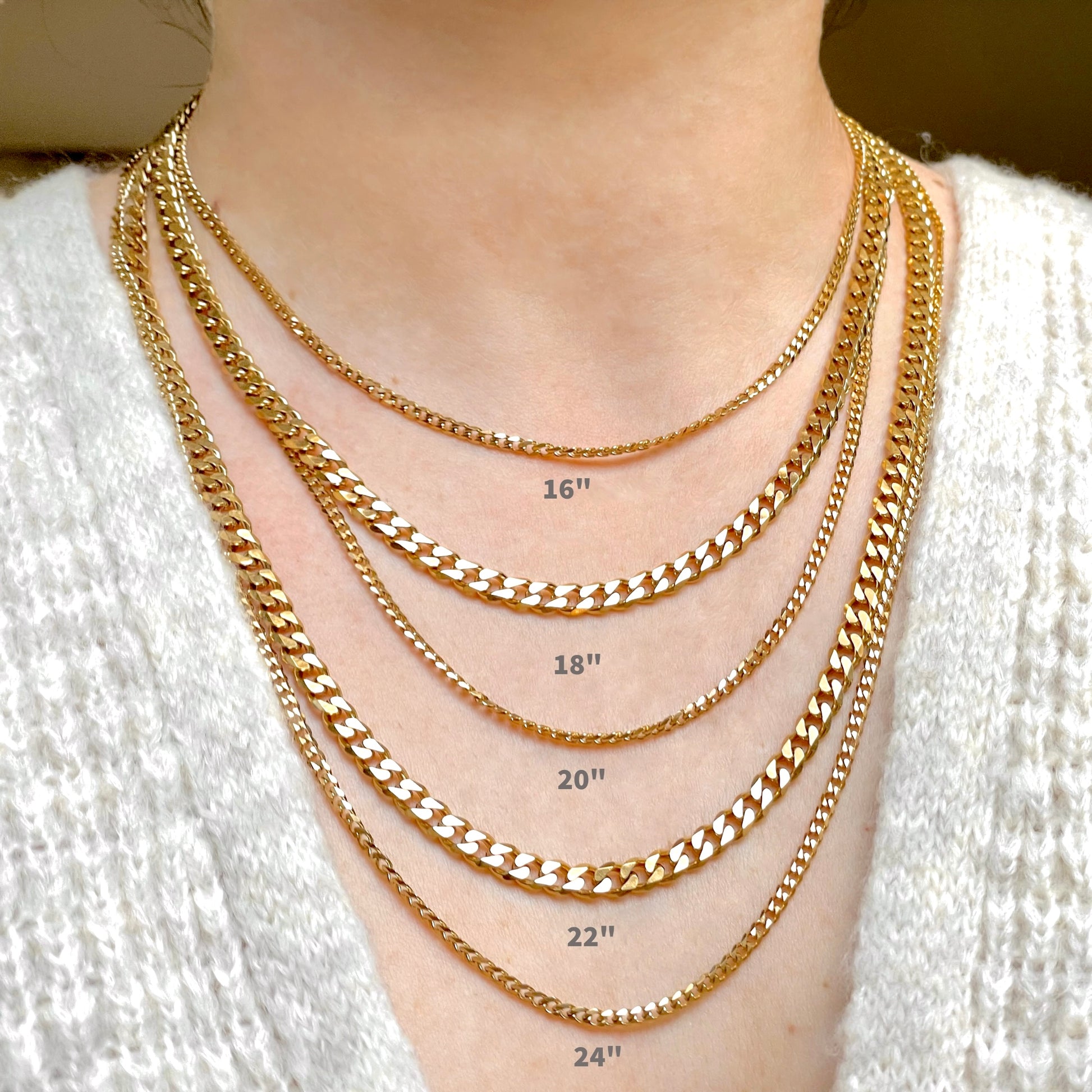 Gold chain necklaces of 5 different lengths and widths displayed on a person wearing a white sweater.