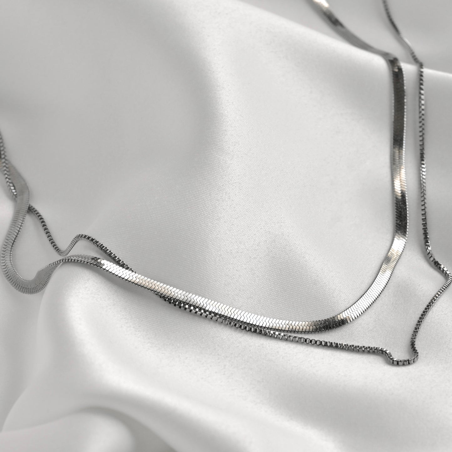 Herringbone and box chain necklace on a white satin background