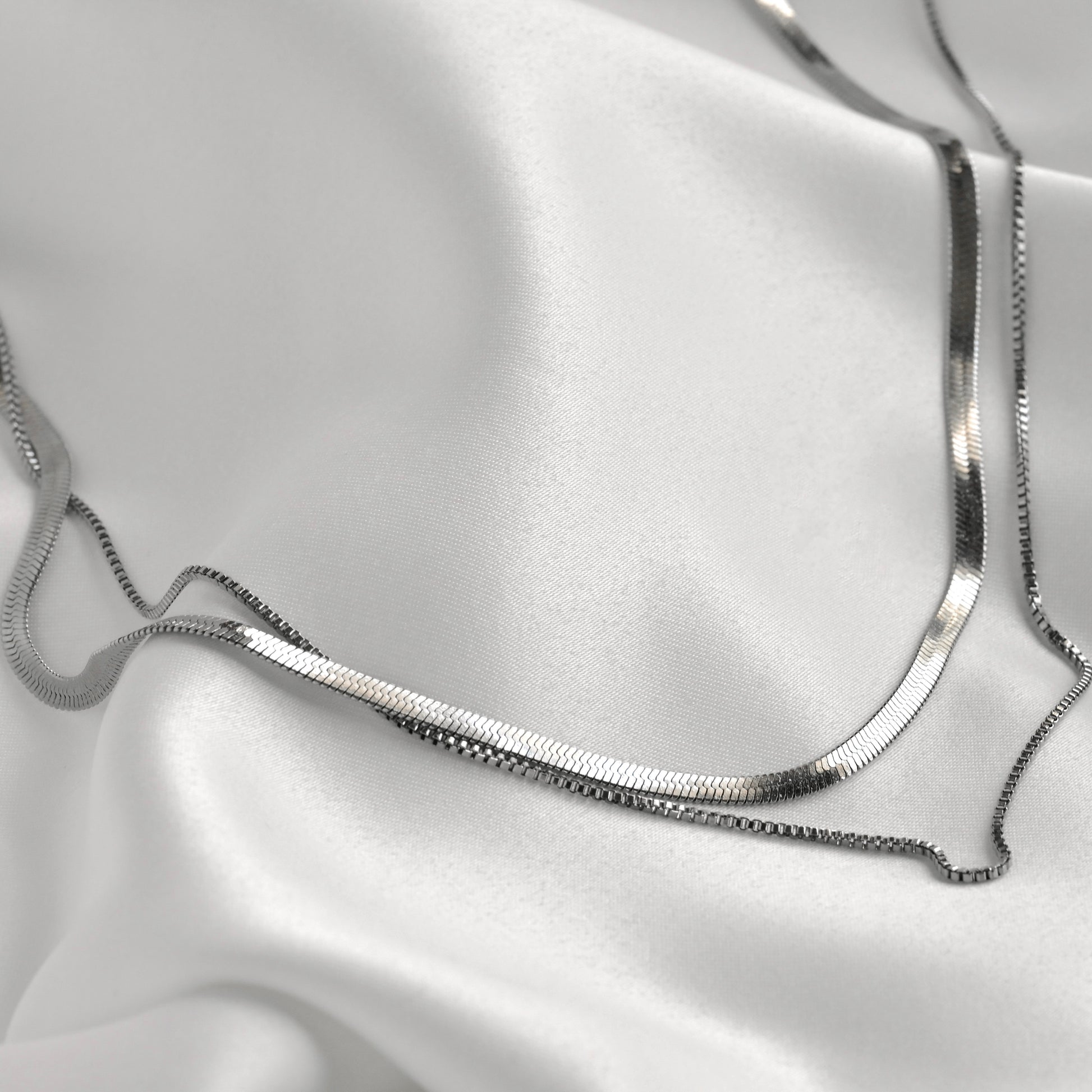 Herringbone and box chain necklace on a white satin background