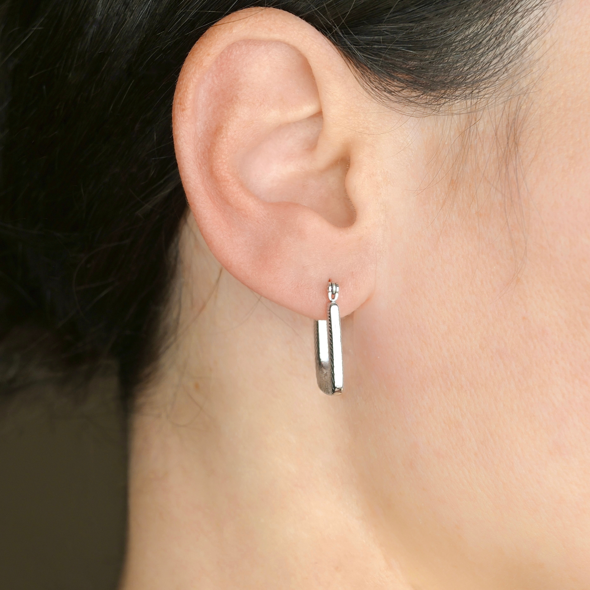 Close-up of an ear wearing a silver square earring with blurred background