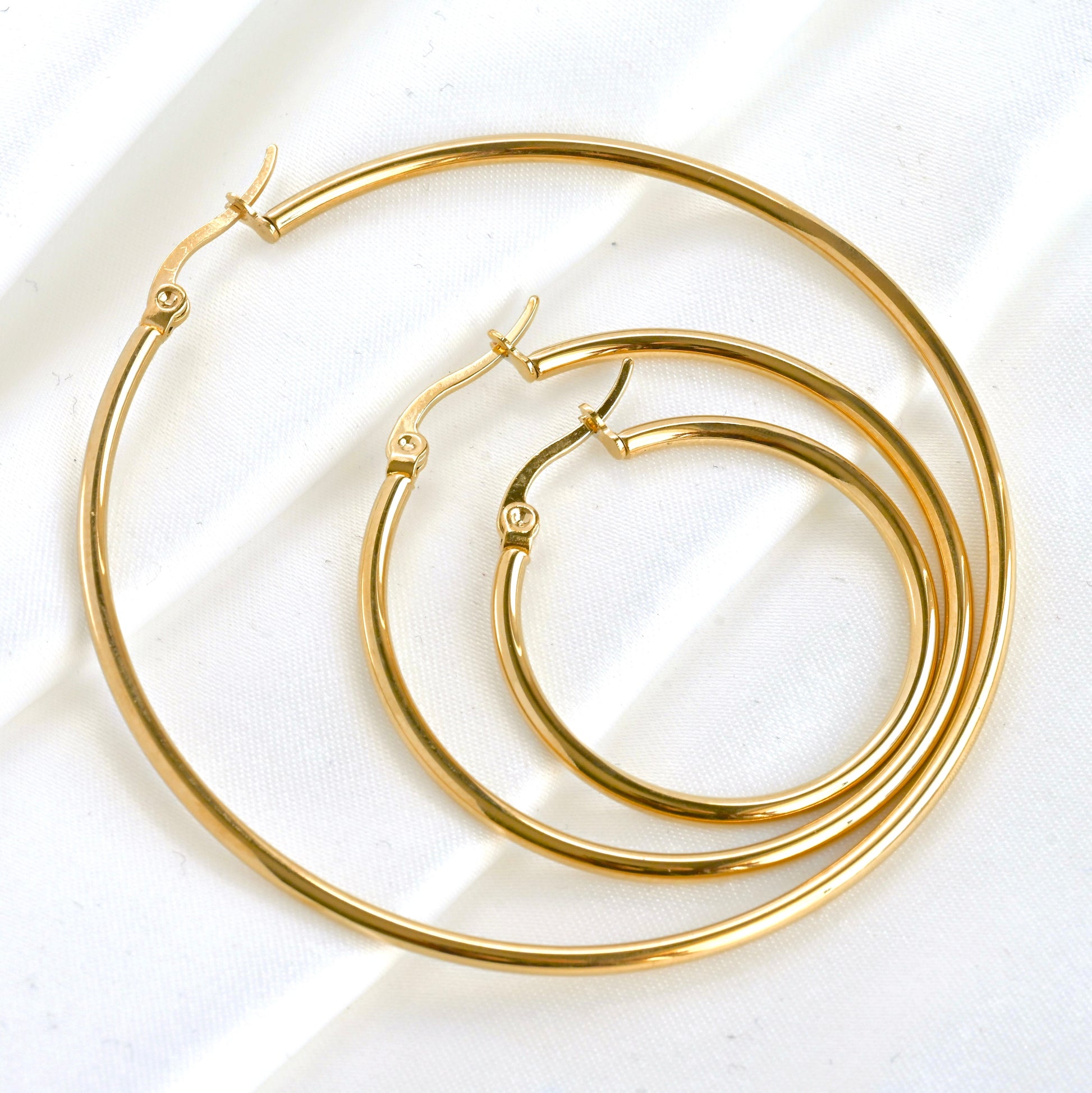 Close-up view of gold hoop earrings in 3 different sizes nested on a white background