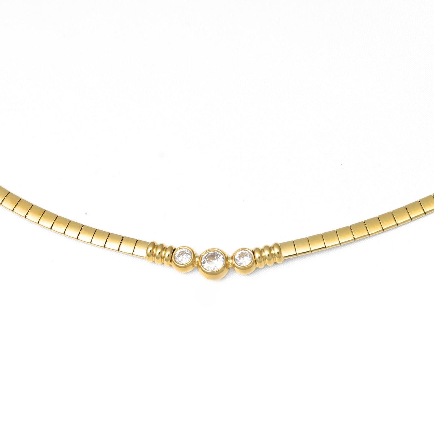 A gold  omega chain necklace featuring three small clear round-cut gemstones set in a central cluster, photographed against a plain white background.