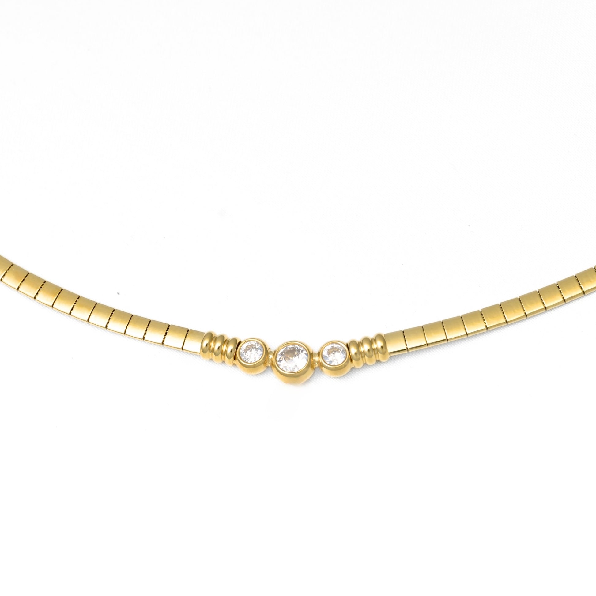 A gold  omega chain necklace featuring three small clear round-cut gemstones set in a central cluster, photographed against a plain white background.