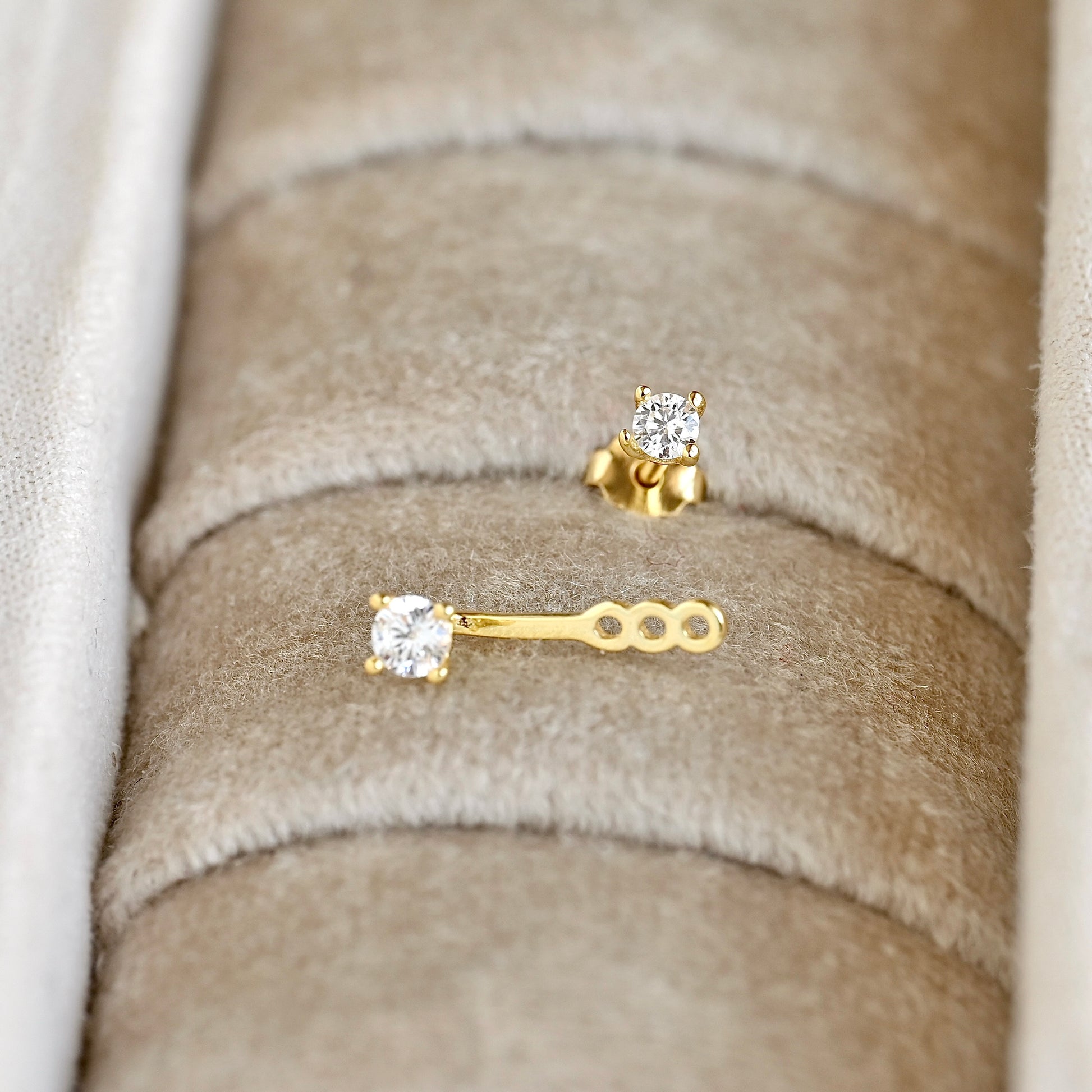 Gold ear jacket with clear CZ stones, one stud with butterfly backing and one jacket style with three slots displayed in a beige jewelry box.