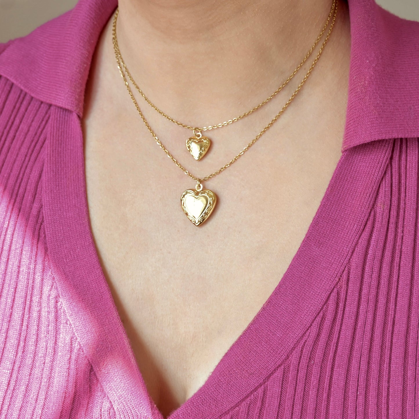 Two gold heart photo lockets, one with big, one with small lockets,  on a person wearing a pink top.