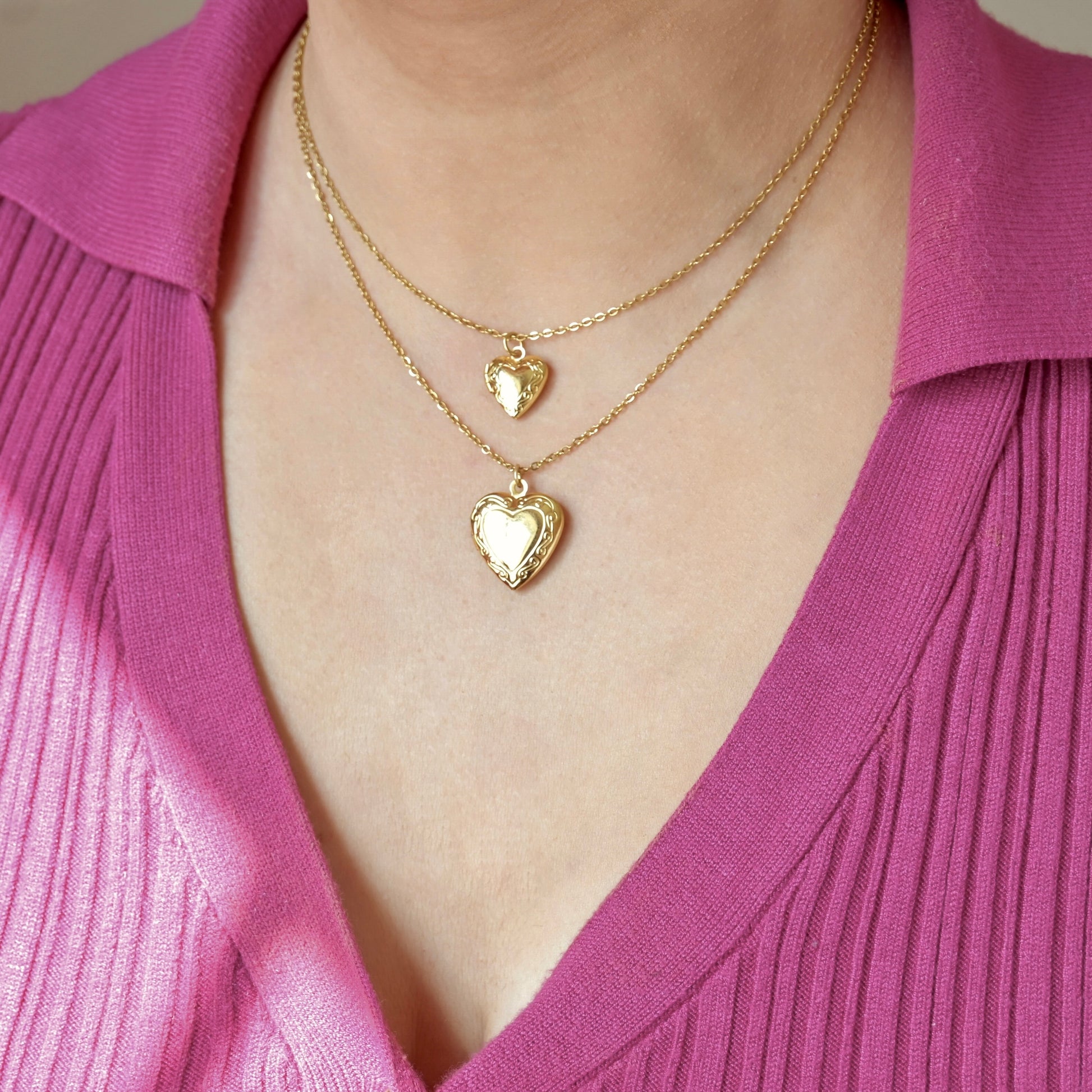 Two gold heart photo lockets, one with big, one with small lockets,  on a person wearing a pink top.