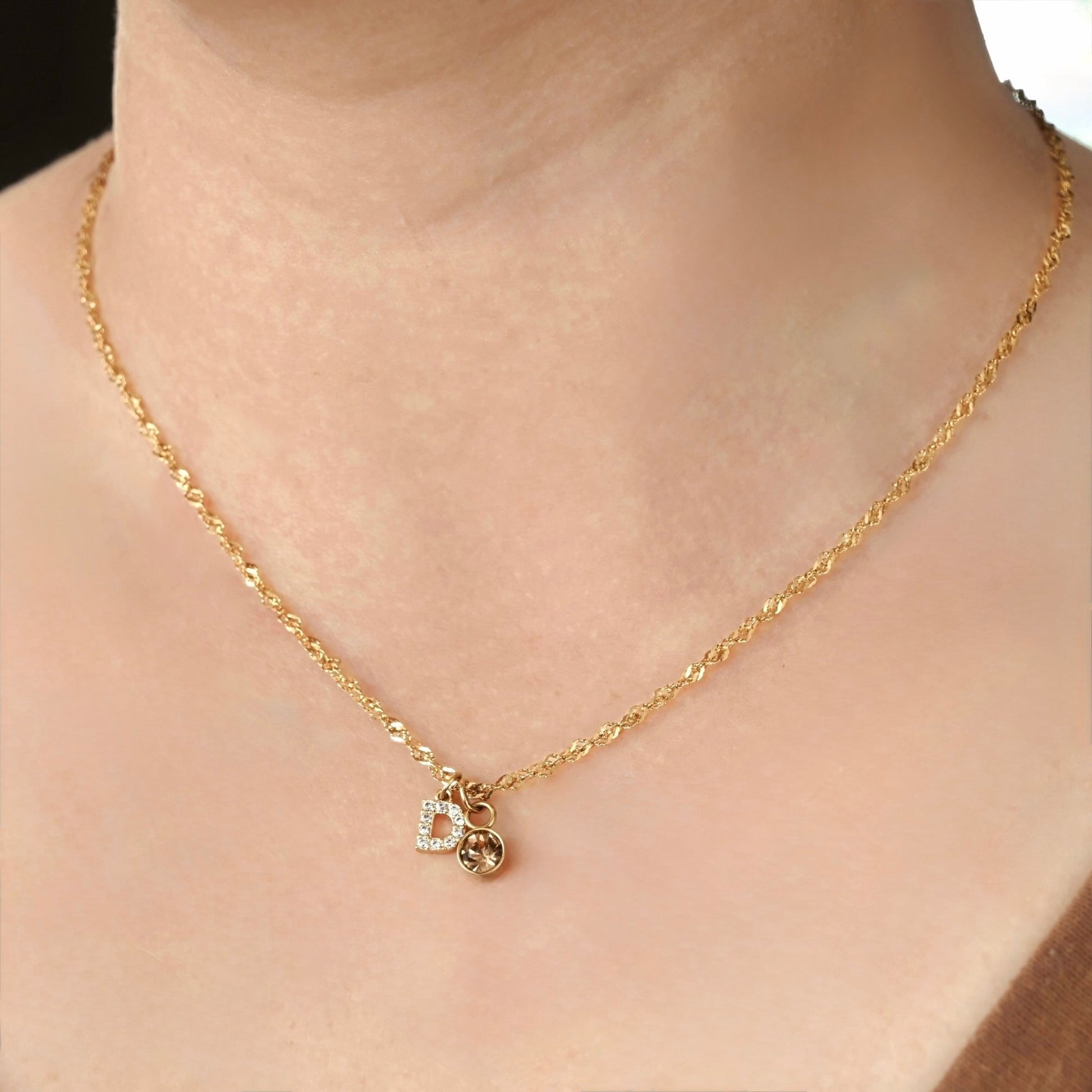 Gold singapore necklace with a letter 'D' pendant  and november birthstone on a person.