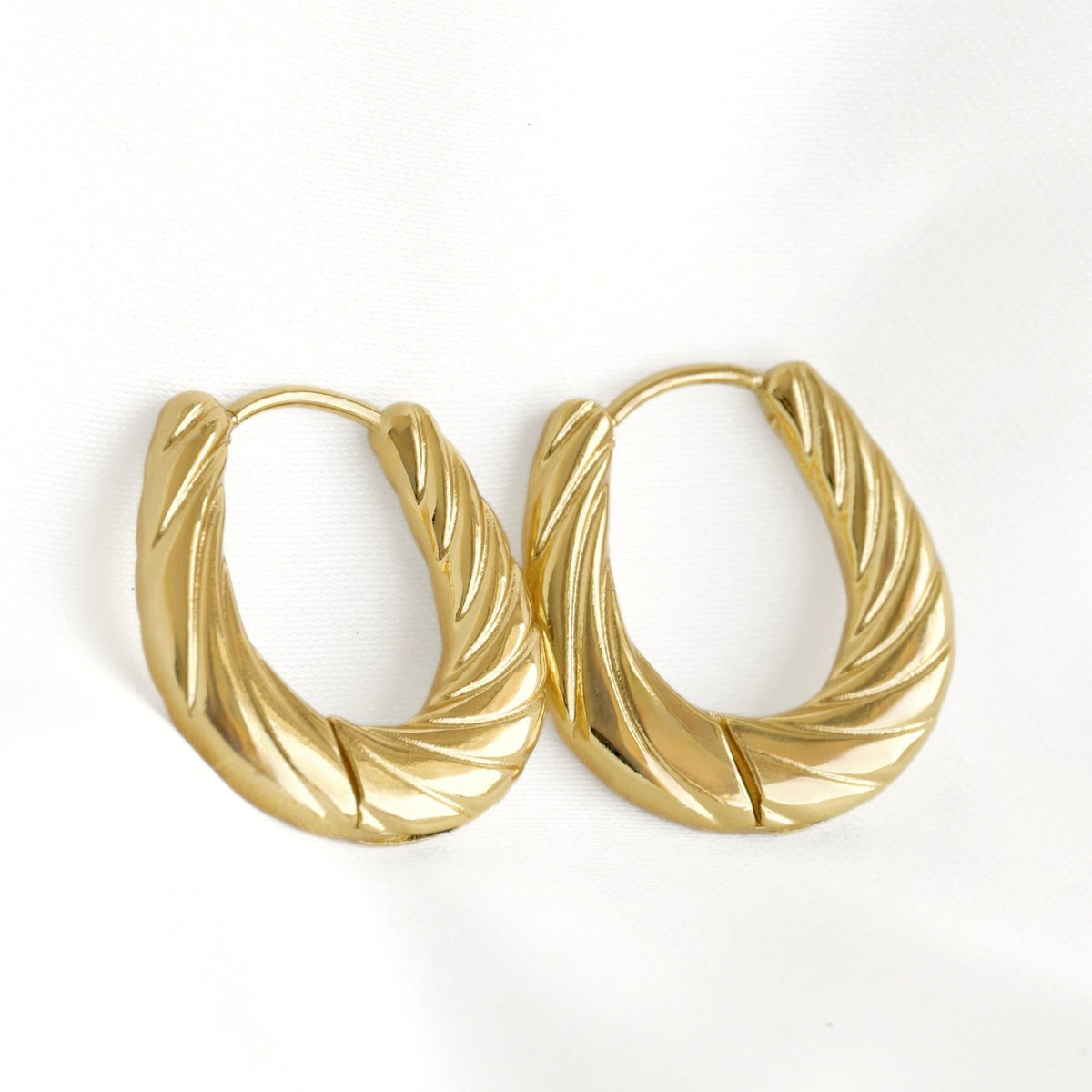 A pair of gold-toned twisted hoop earrings with a textured, ribbed surface, displayed on a clean white background.
