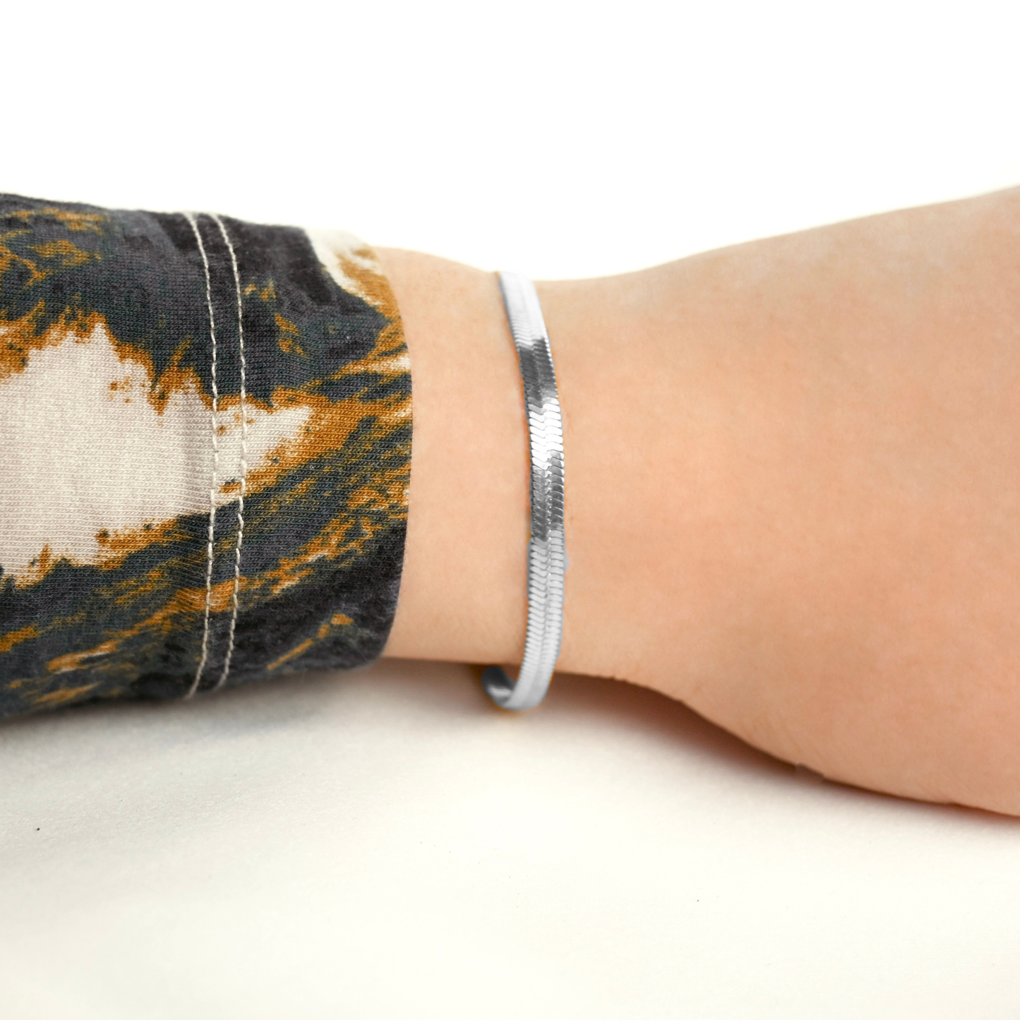 Bold silver herringbone bracelet on a wrist with a patterned sleeve against a white background