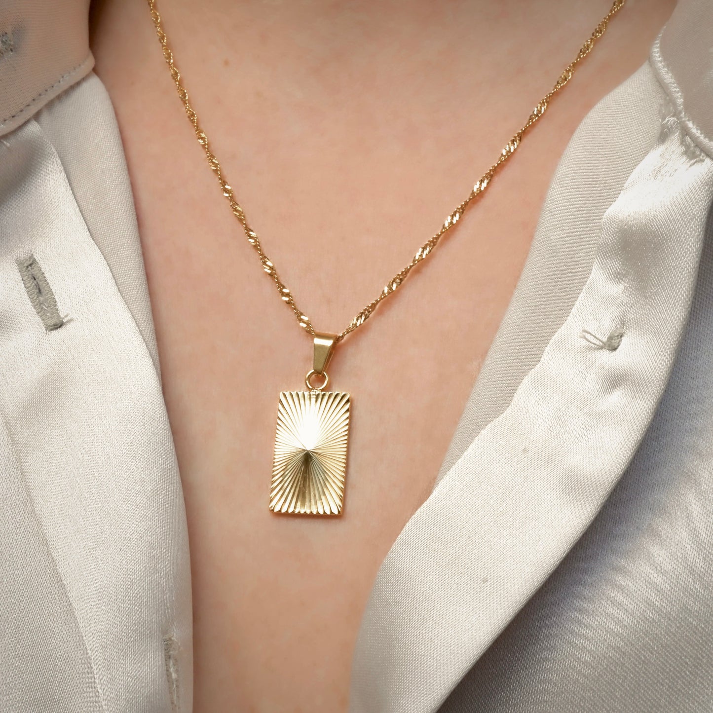 Gold sunburst pendant with ribbed radial ribbed texture worn by a person in a light-colored outfit.