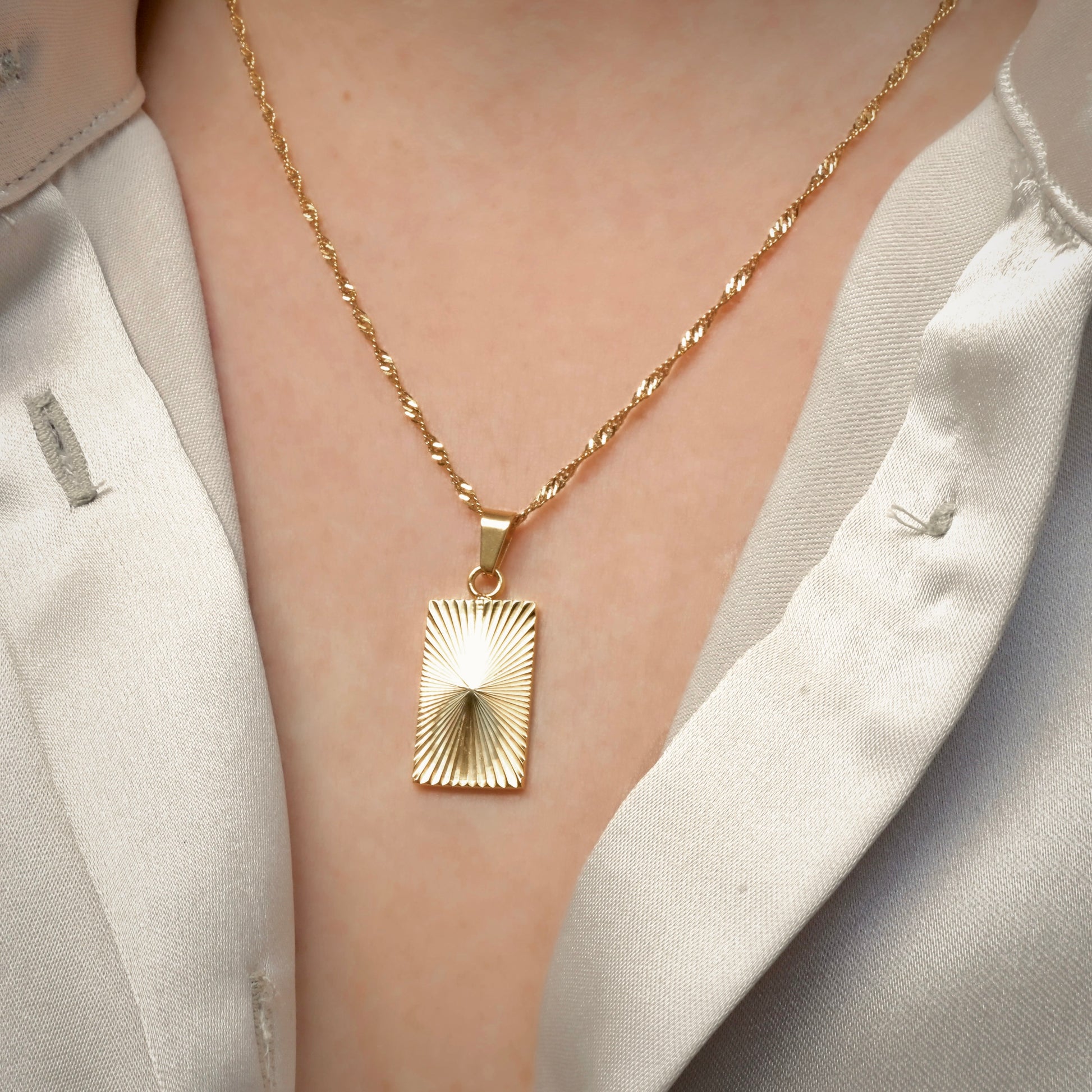 Gold sunburst pendant with ribbed radial ribbed texture worn by a person in a light-colored outfit.