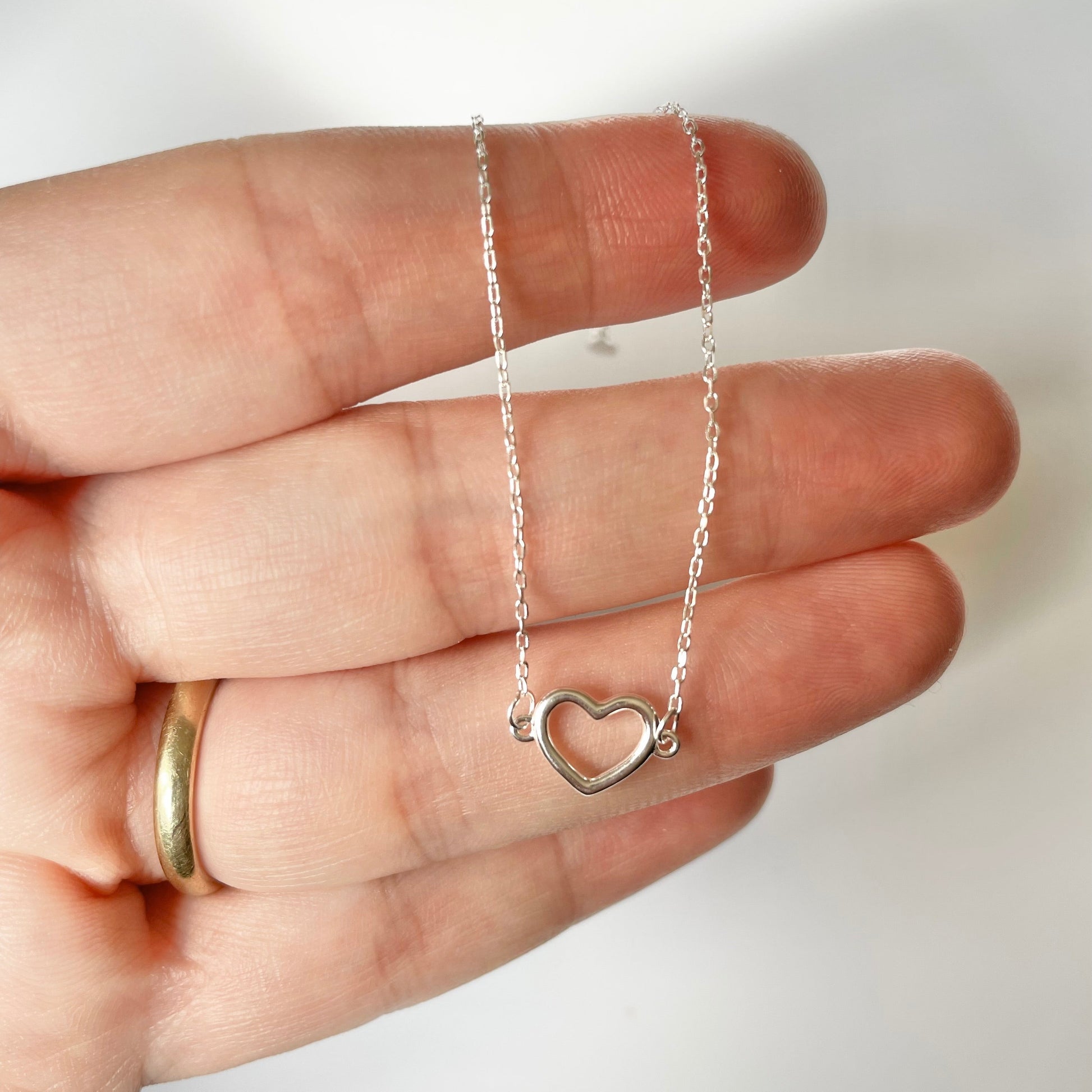 Silver heart bracelet with a delicate chain held in a hand against a white background