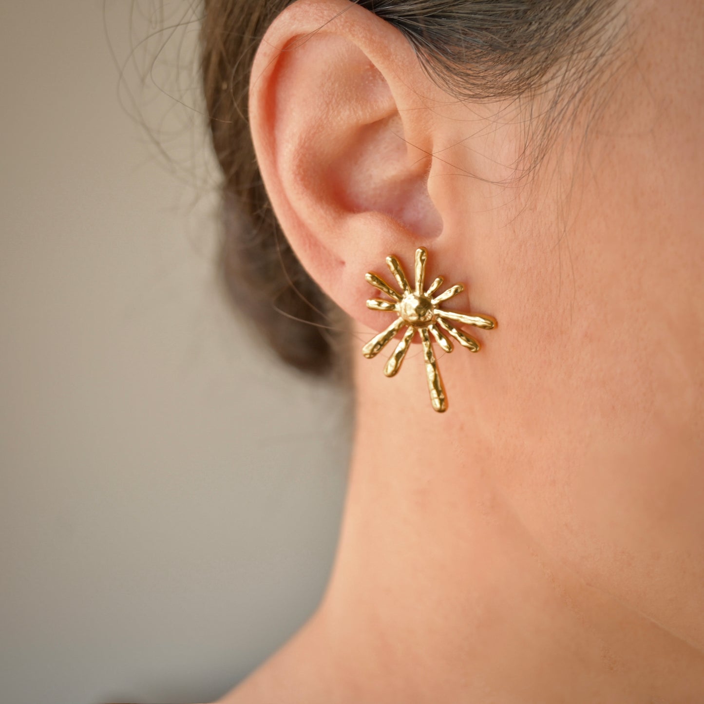 oversized gold sunburst earrings  worn by a person
