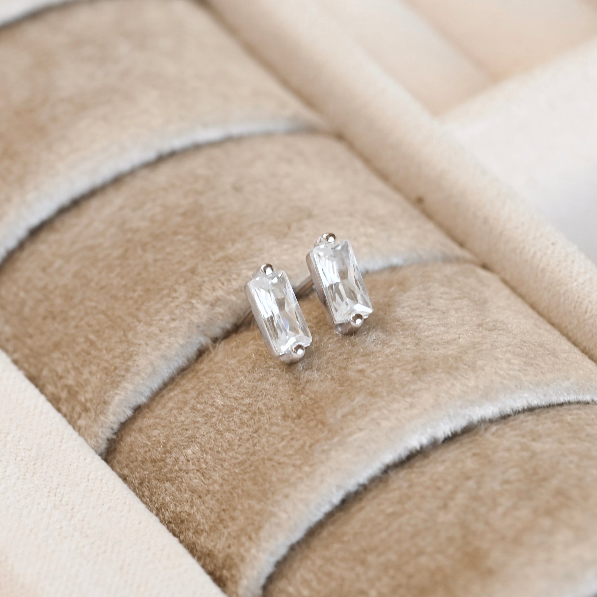 Pair of silver CZ bar stud earrings with clear gemstones on a beige cushion