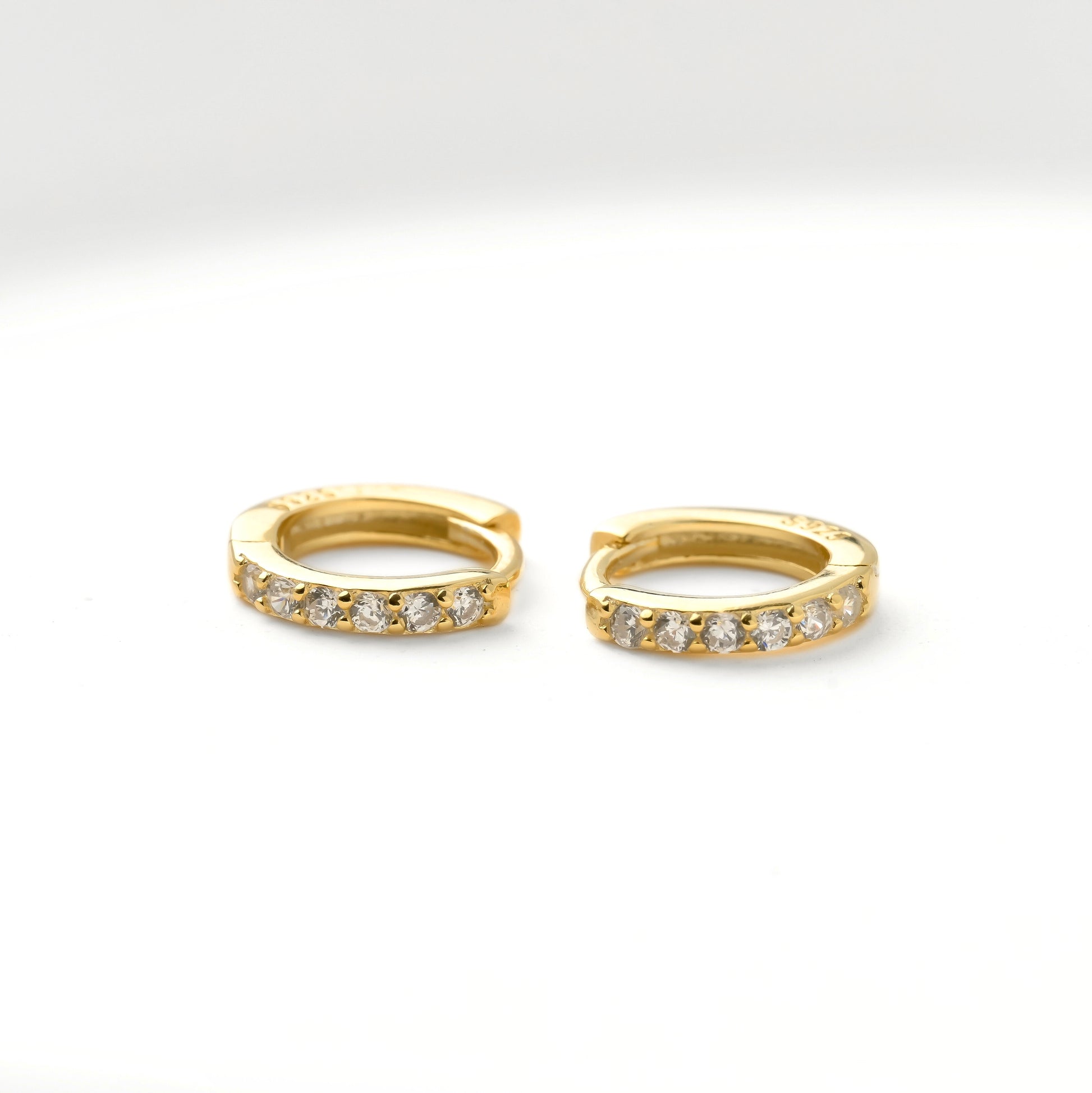 Gold huggie hoop earrings with embedded diamonds and S925 hallmark stamp on a white background