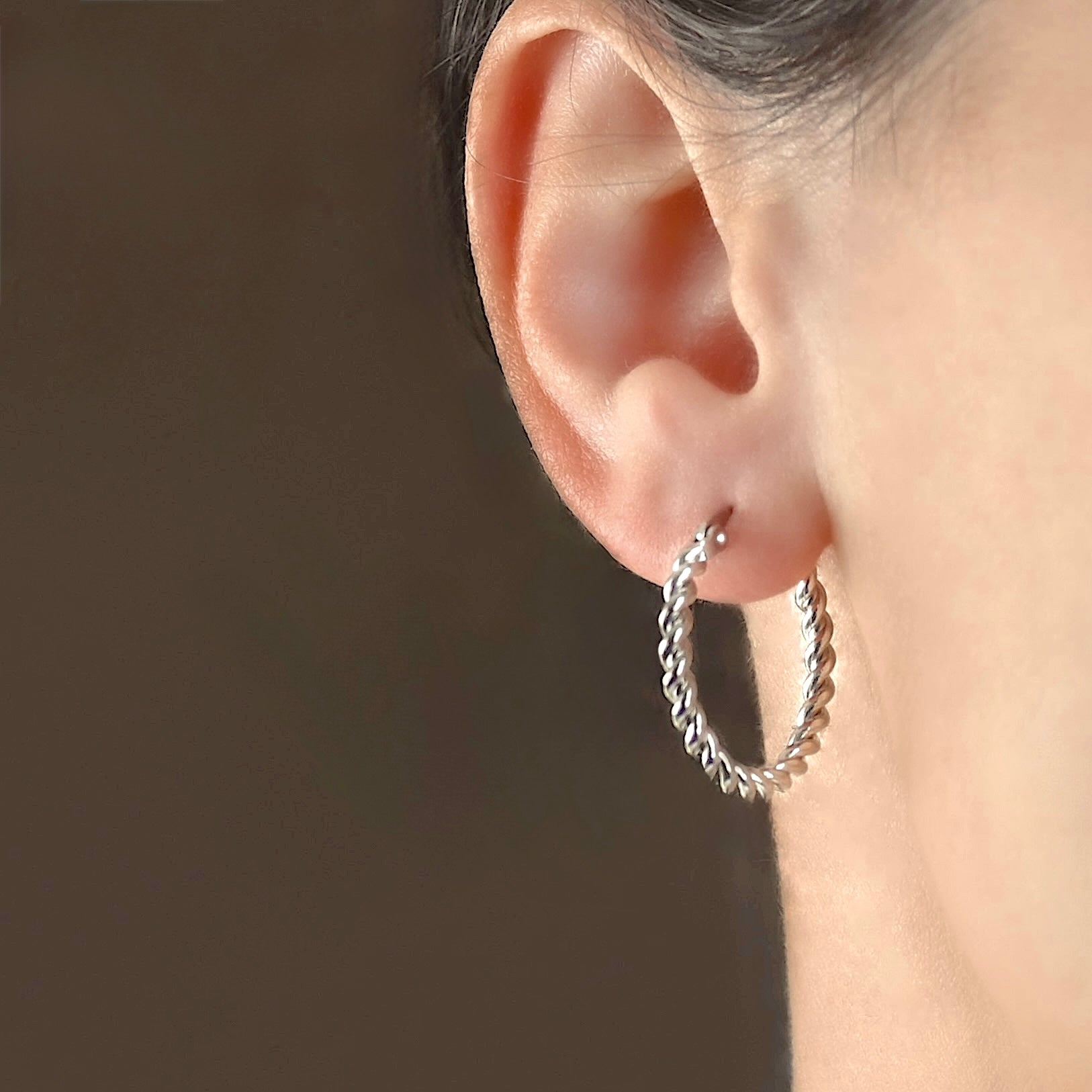 Dainty silver  twist hoop earrings worn by a person with a dark background