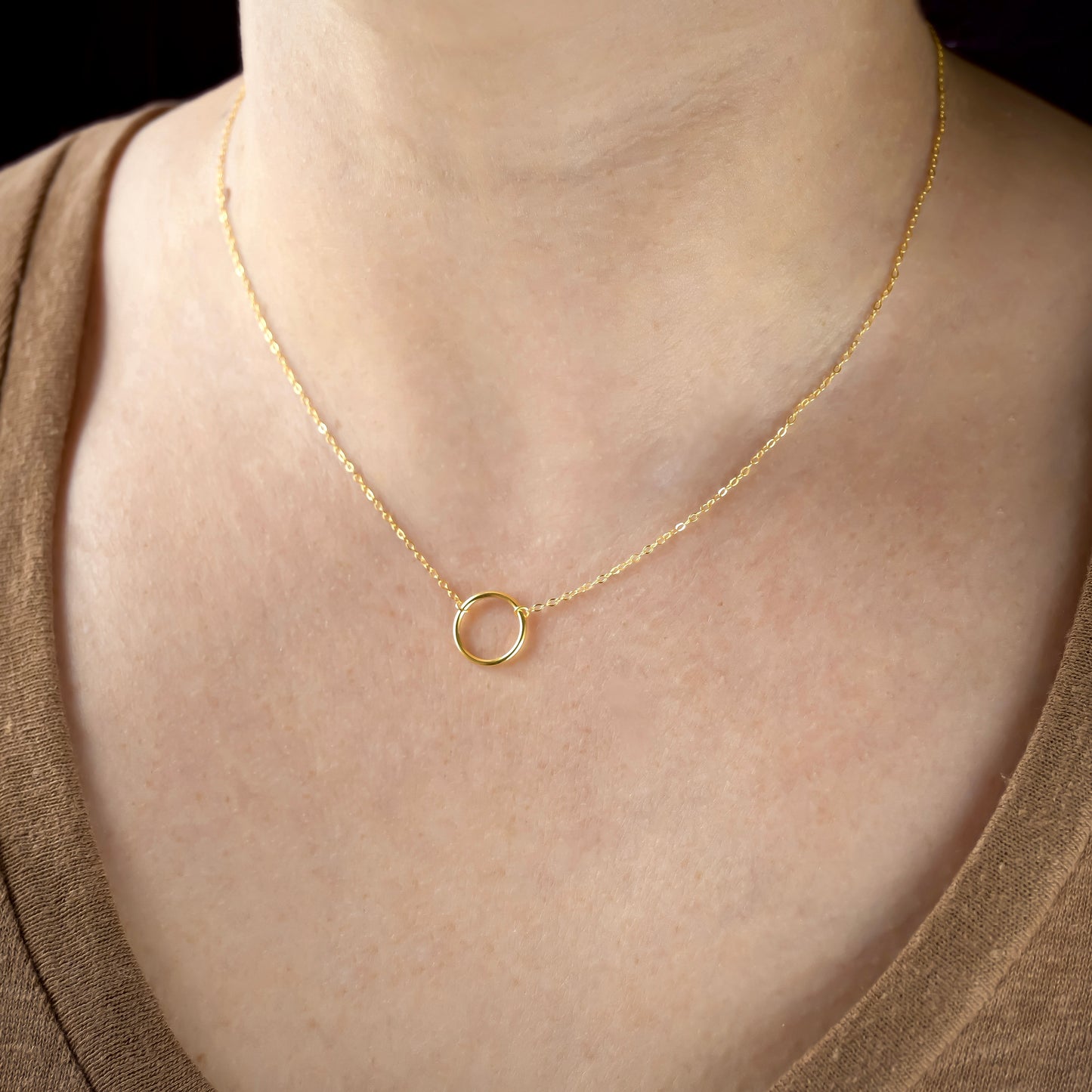 Gold necklace with a small ring pendant on a person wearing a brown top.