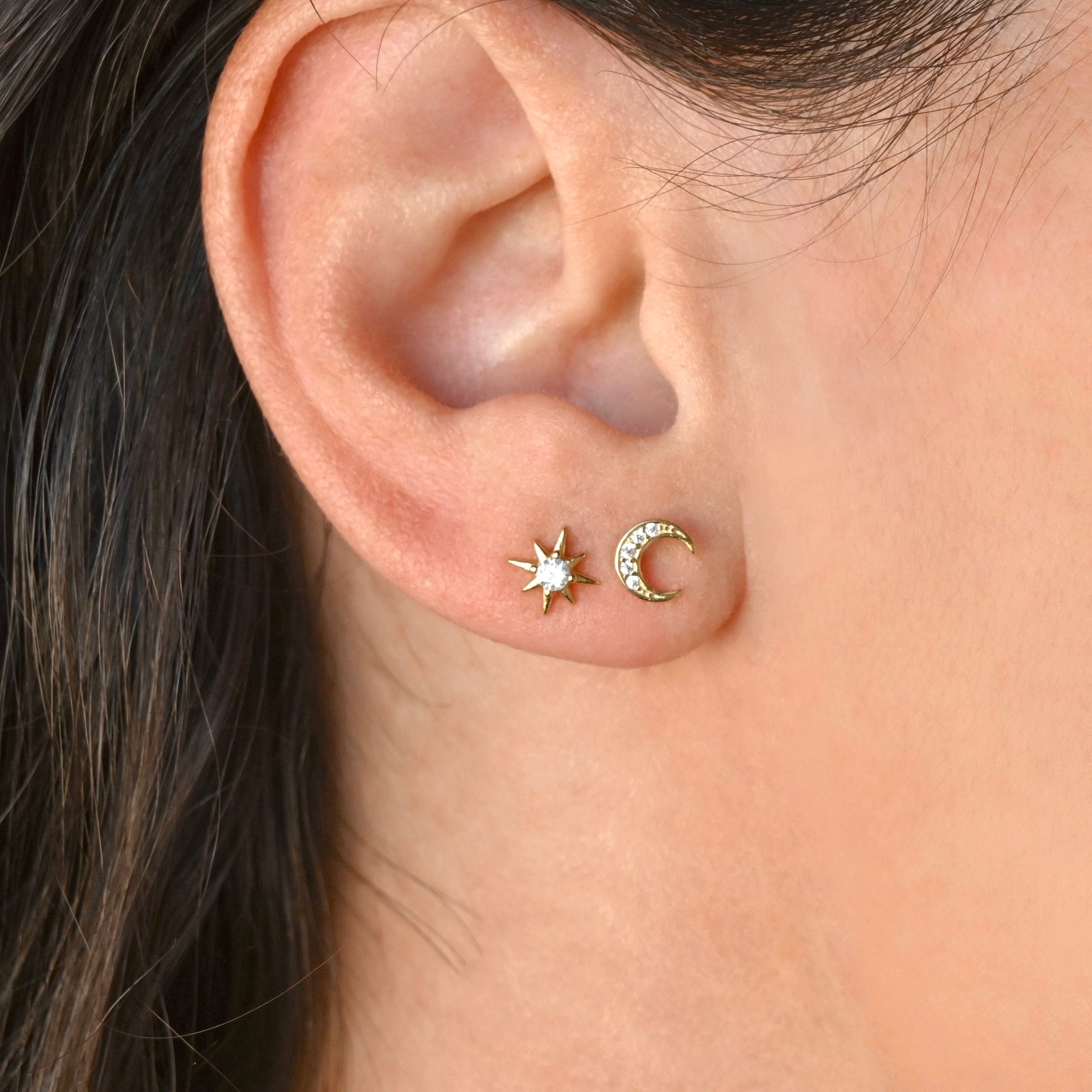 Close-up of an ear wearing gold star and moon stud earrings.