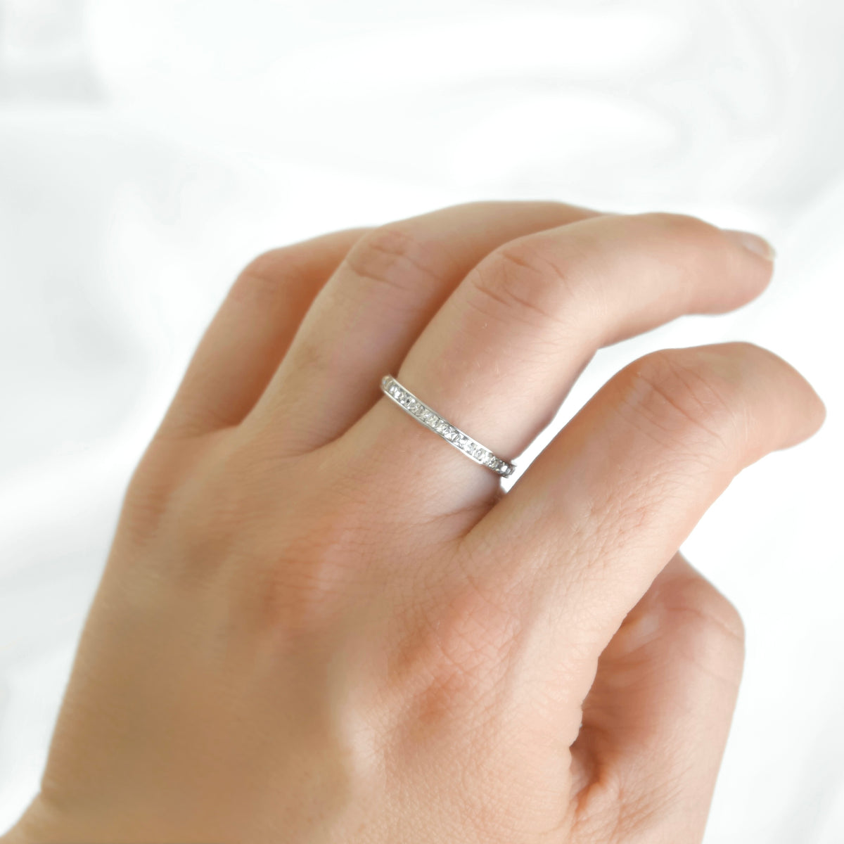 Slim silver eternity ring with channel set squre cubic zirconia stones on a woman's middle finger.