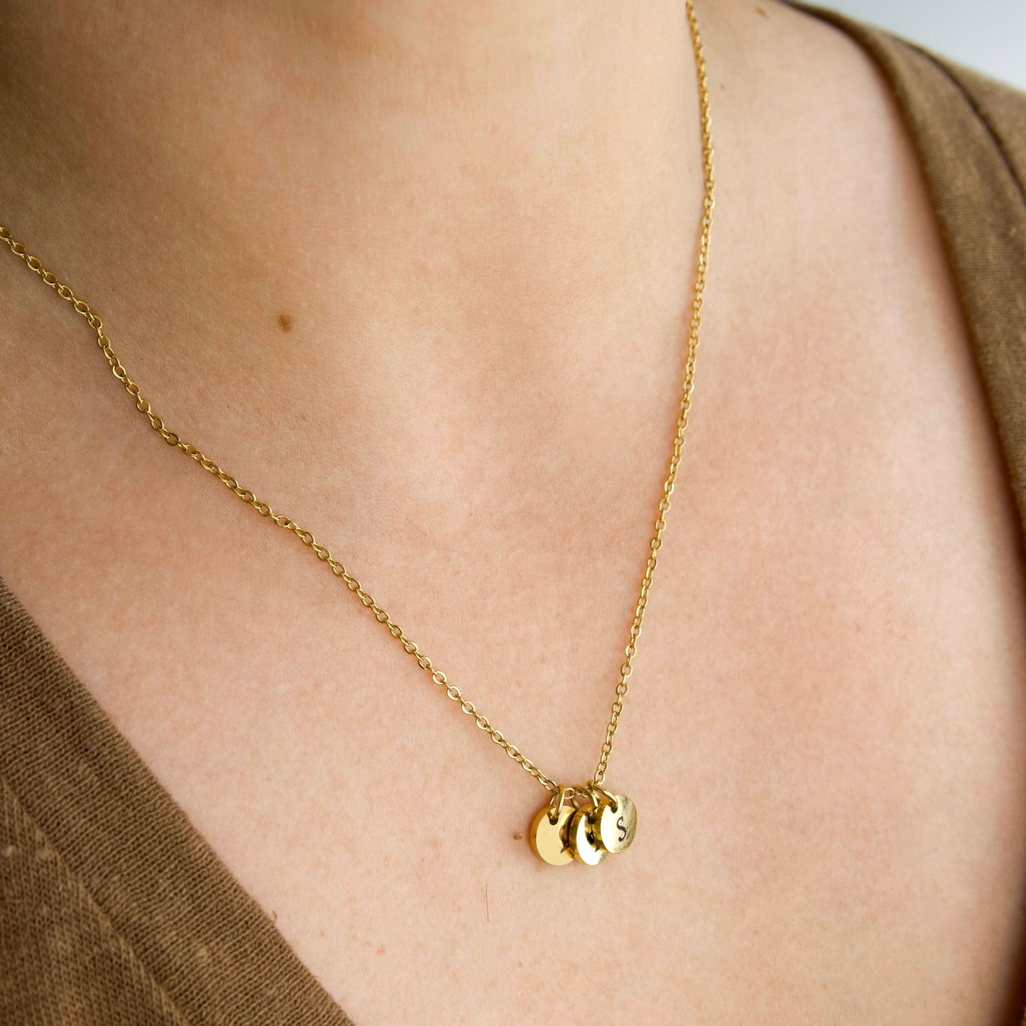 20" gold necklace personalized with three gold disc letter pendants on a person wearing a brown top.