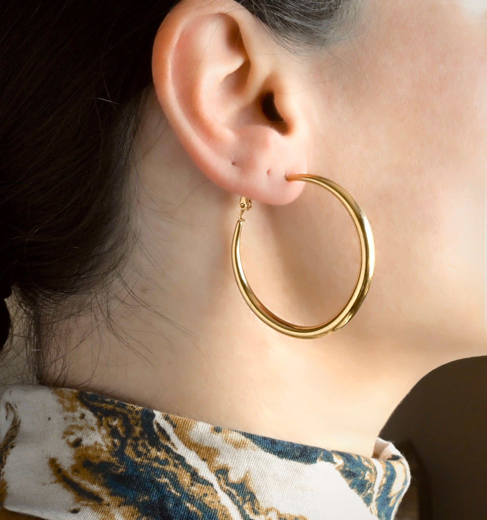 Side view of tapered gold hoops worn by a person with a blurred background