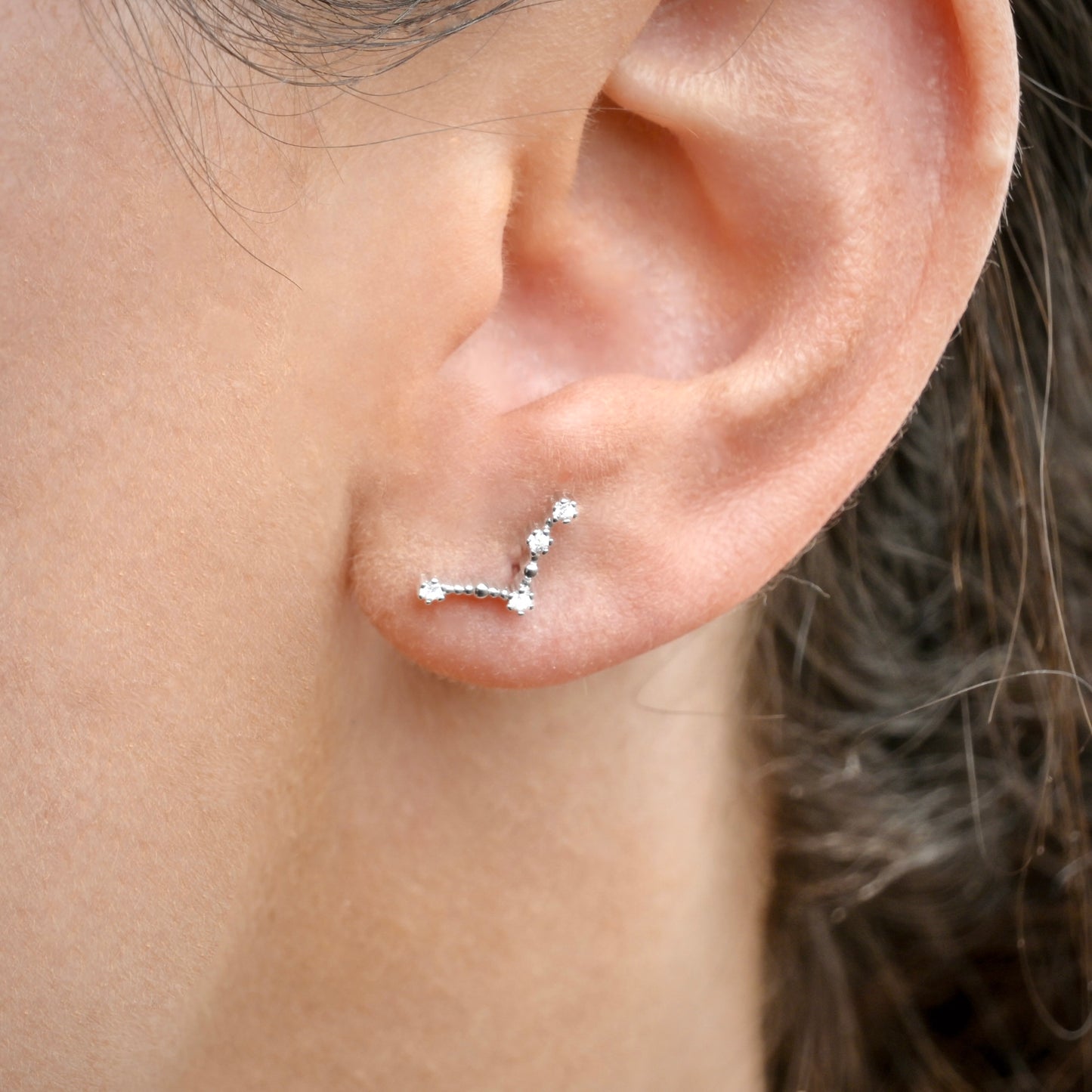 Close-up of an ear wearing a silver aries constellation stud.
