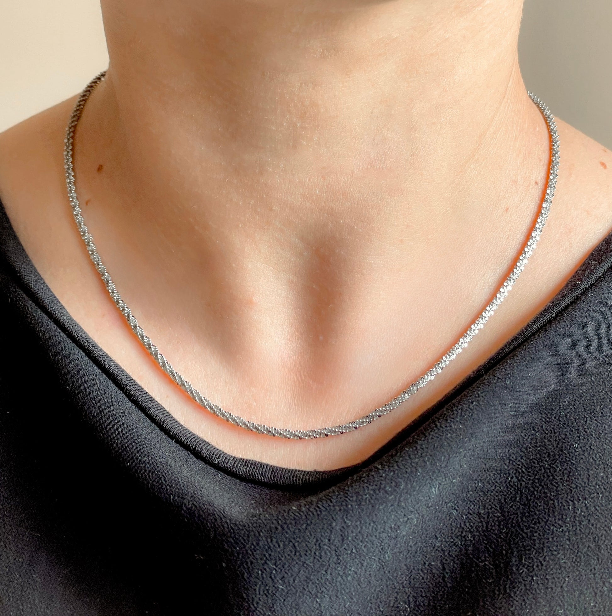 Silver chain on a person wearing a black top against a neutral background