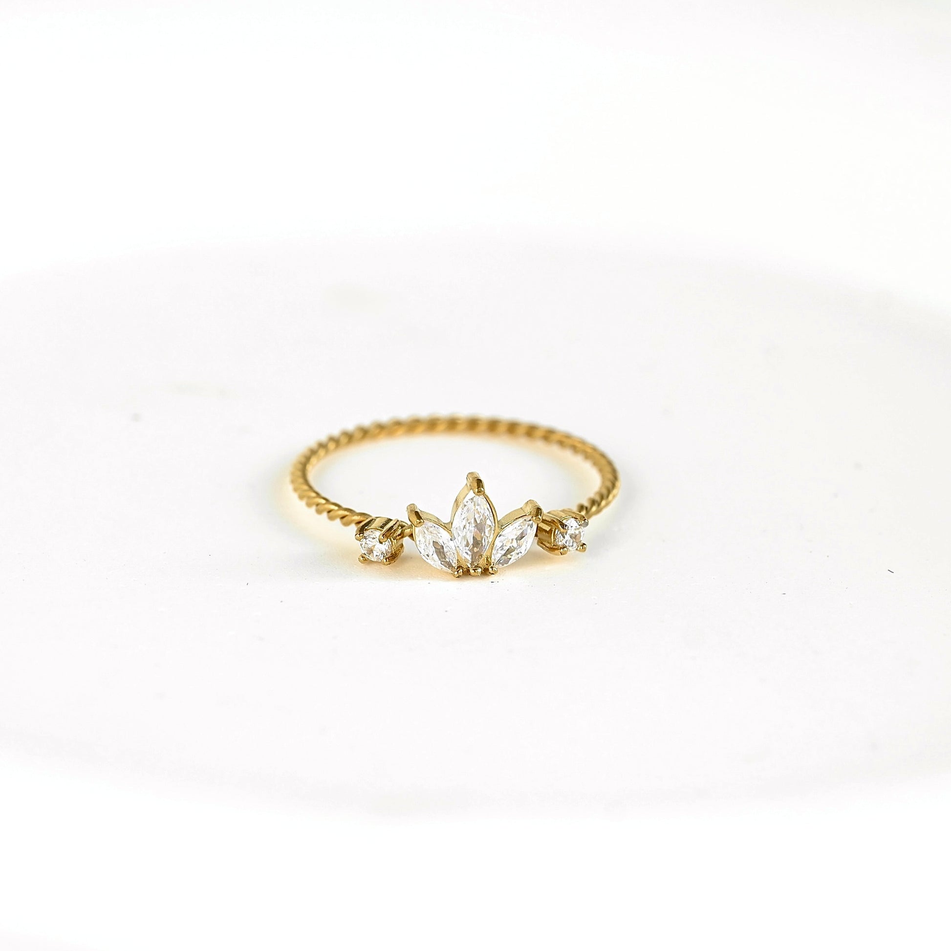 A yellow gold ring featuring a marquise-cut center stone and smaller side stones, set on a textured twisted band, photographed on a plain white background.