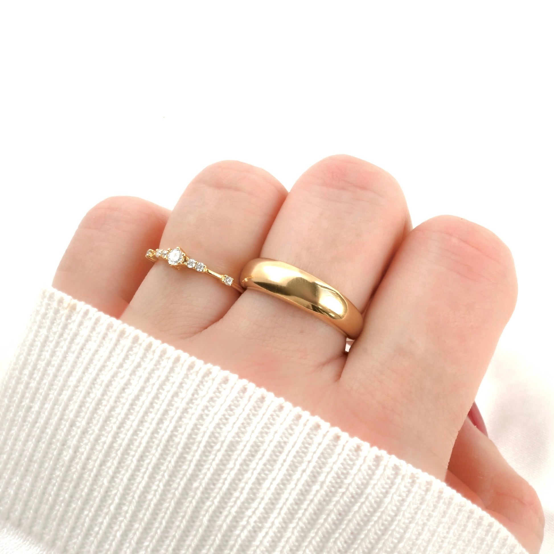 Gold dome ring with a diamond cluster ring side by side on a finger with a white background