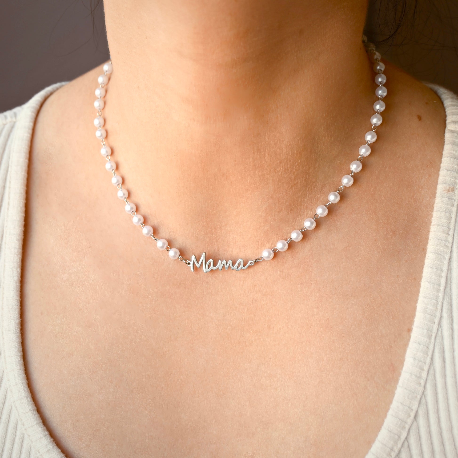 A close-up of a person wearing a pearl necklace with a silver script nameplate that reads 'Mama'.