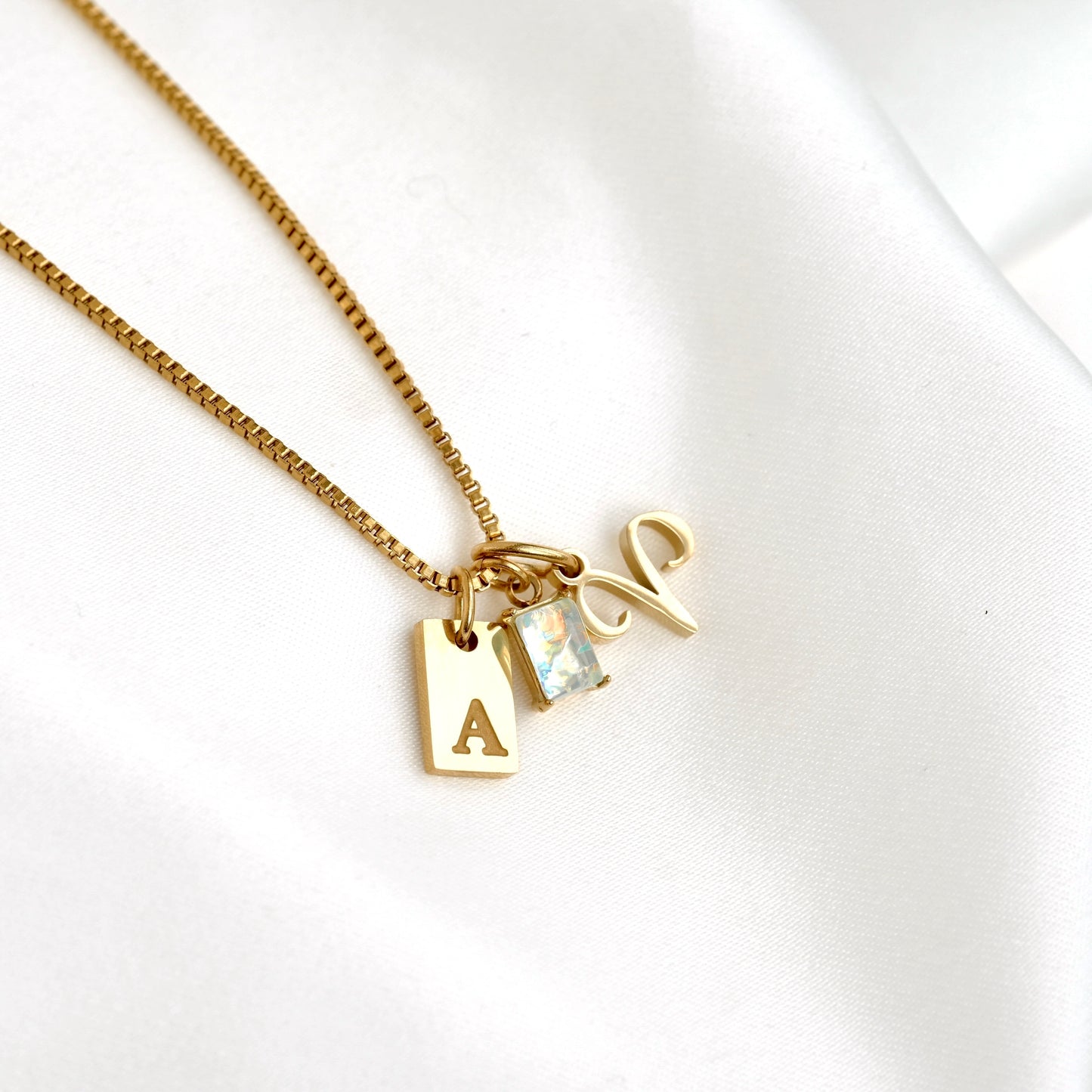 Gold necklace with letter 'A' and gemstone charm on a white background