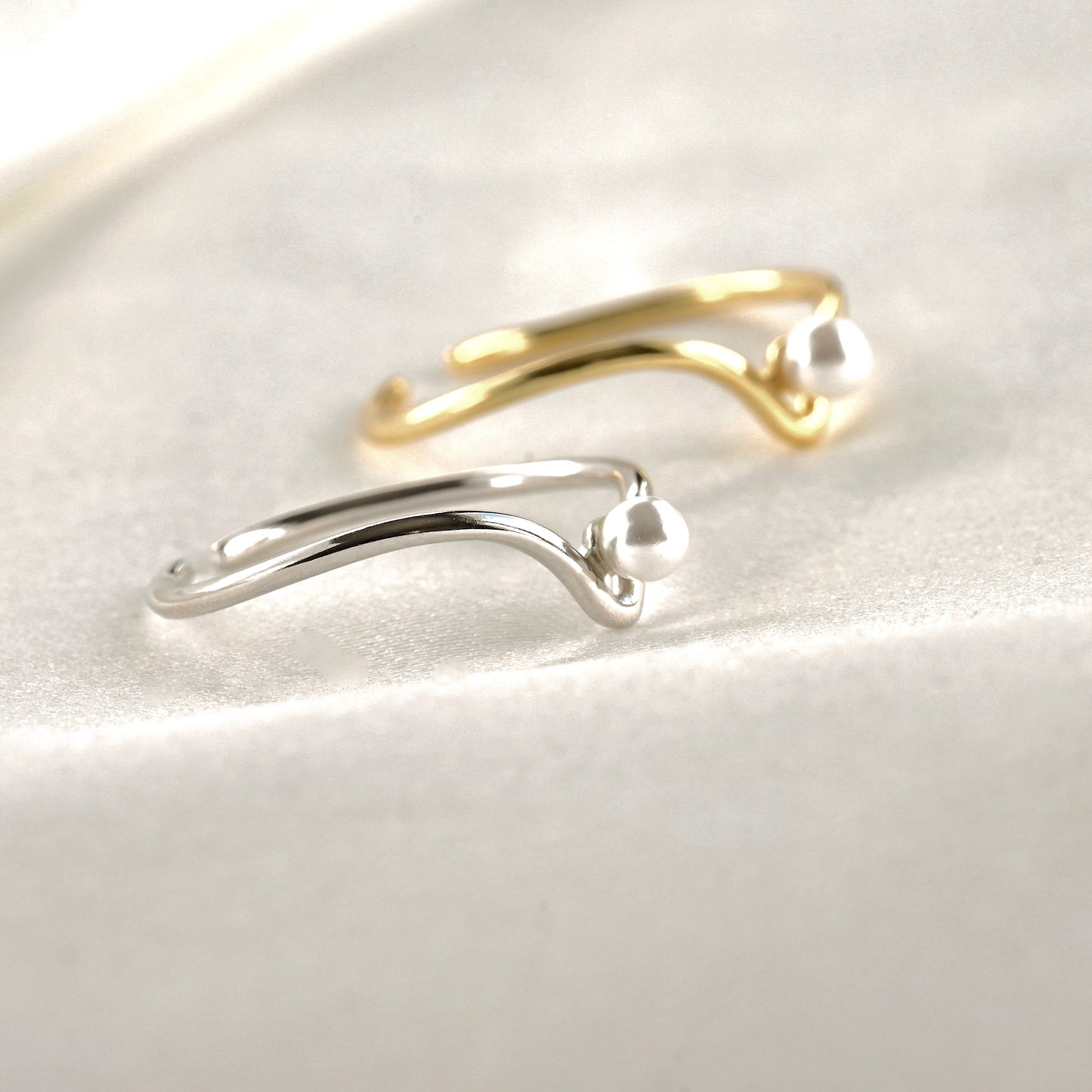 Side view of gold and silver open pack pearl wishbone rings on a light gray background