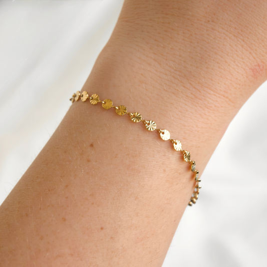Gold coin chain bracelet on a wrist against a white background
