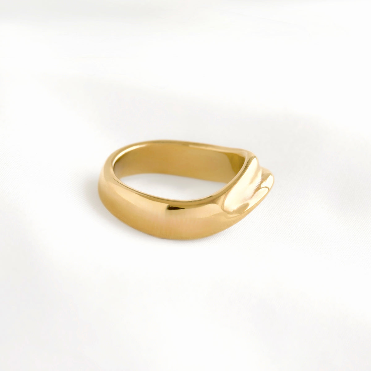 A polished yellow gold ring with a unique, organic wavy shape, photographed on a clean white textured fabric background.