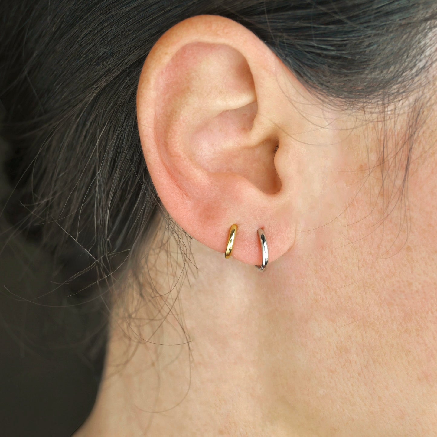 Close-up of an ear wearing two gold hoop earrings , one gold and one silver, with a blurred background.