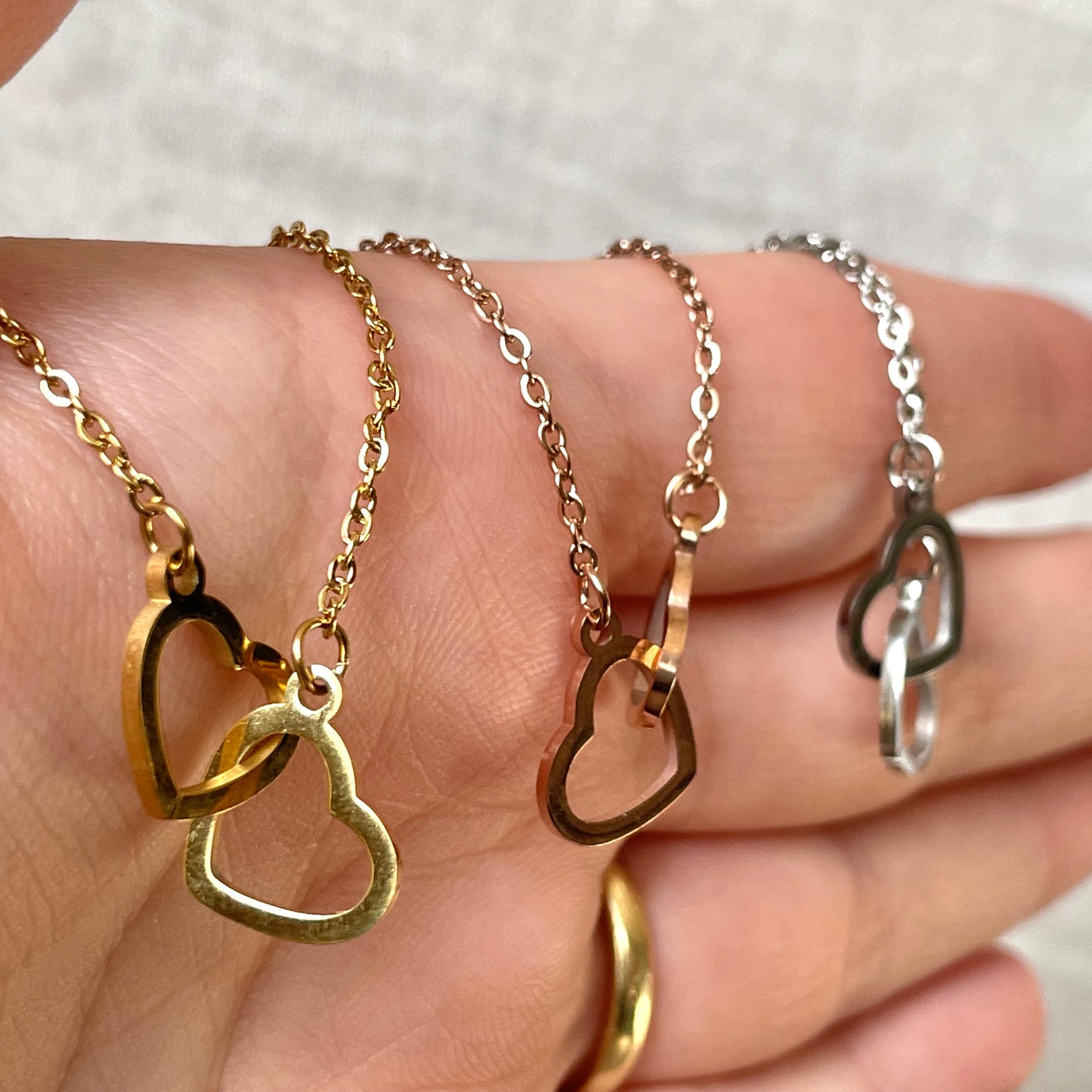 Three heart pendants on gold, rose gold and silver chains held in a hand.