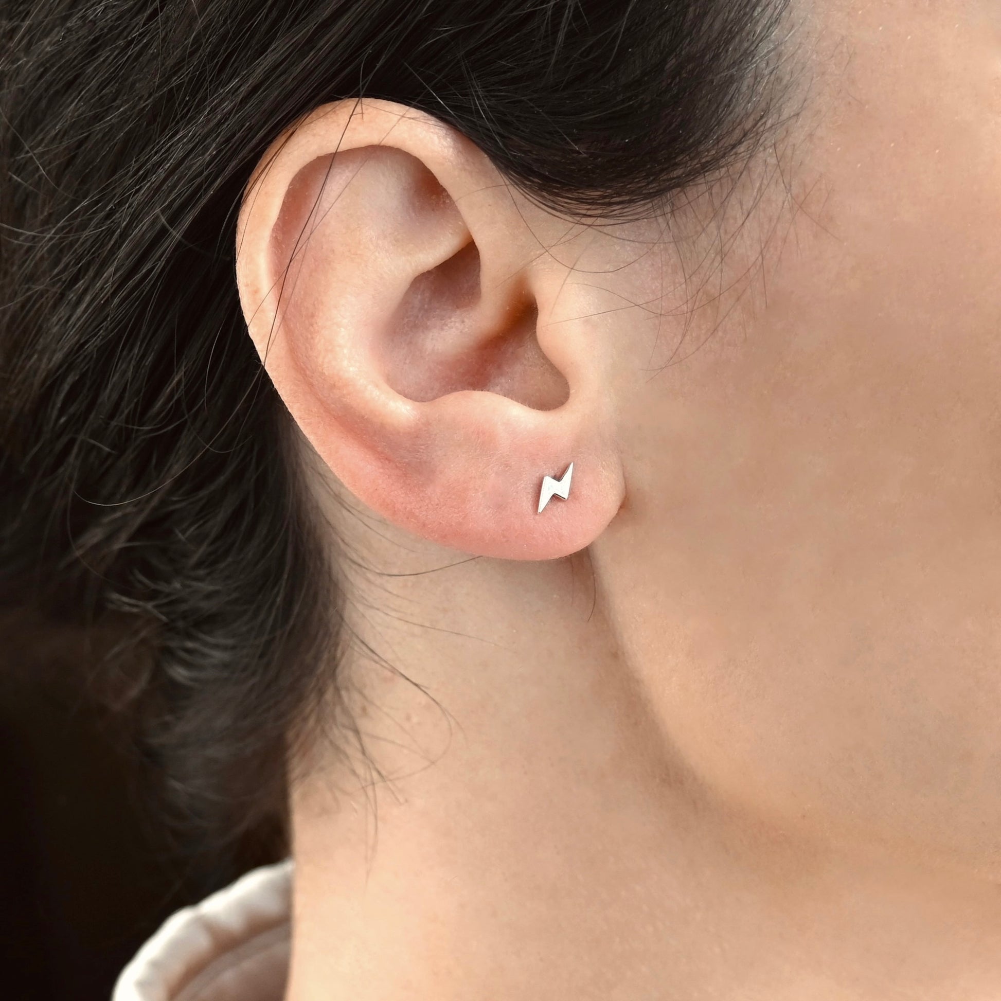 Close-up of an ear wearing small silver thunder bolt stud earrings 
