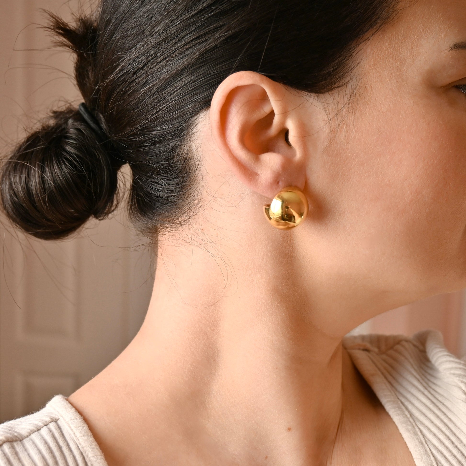A close-up side profile of a woman wearing a small, polished gold dome stud earring.