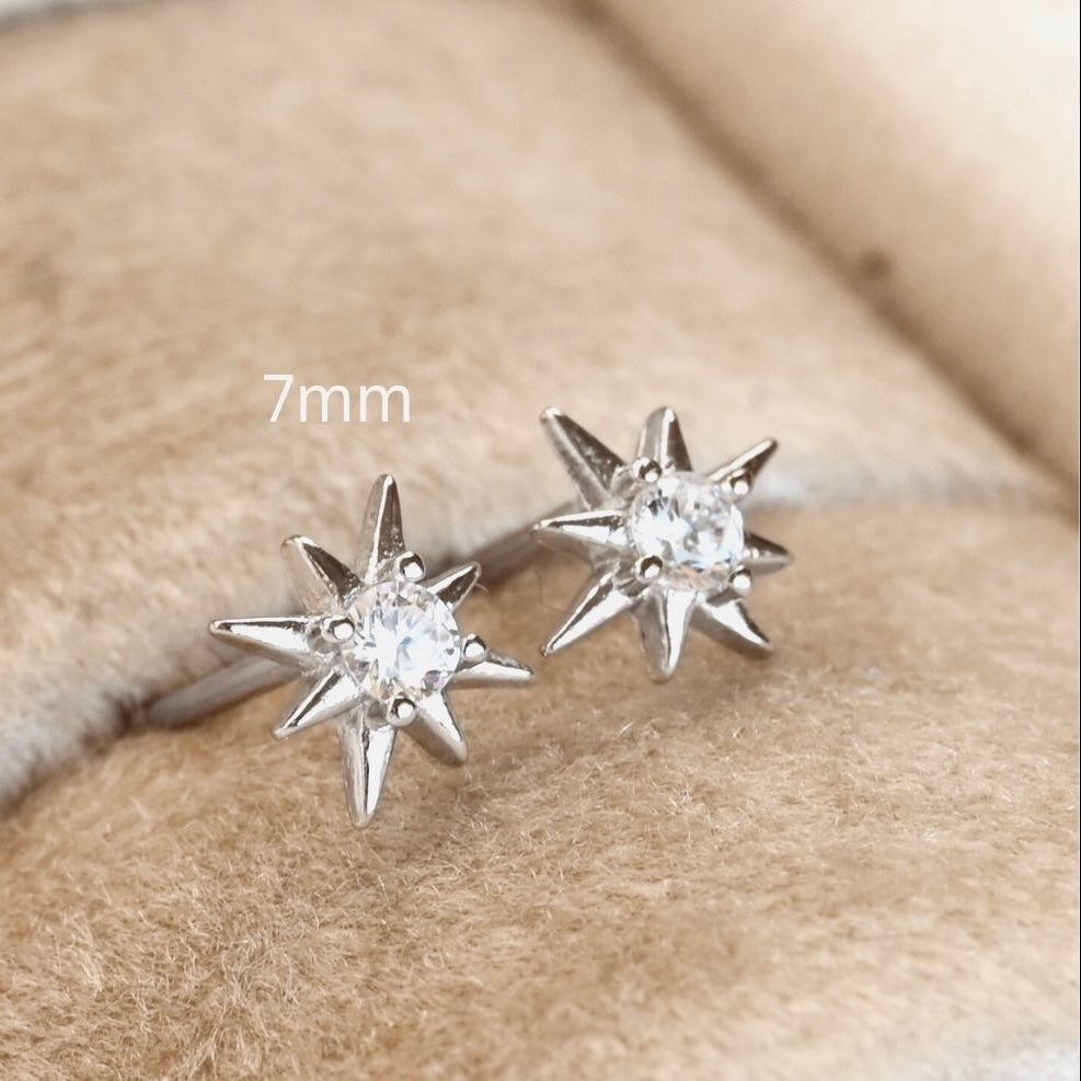 Silver starburst earrings with clear gemstones on a beige fabric background.