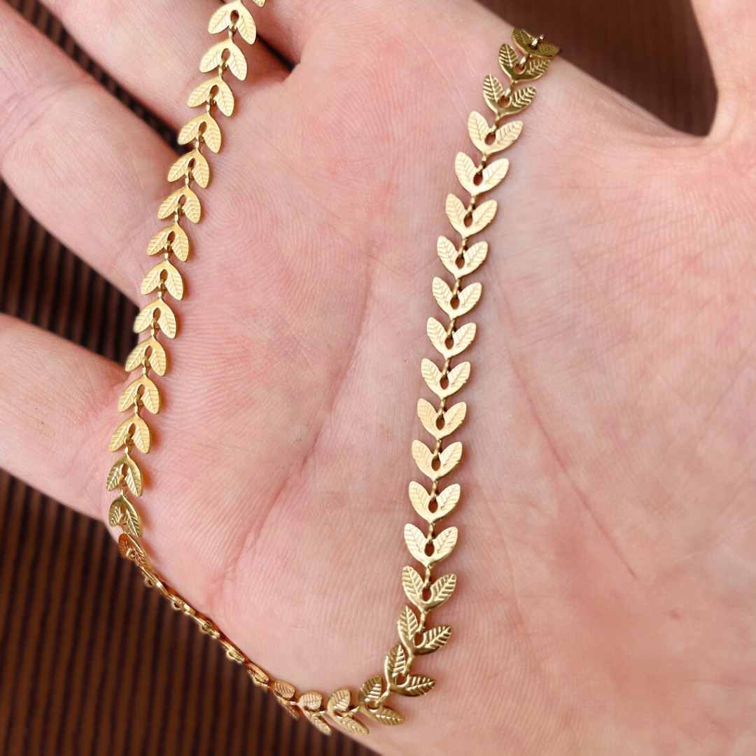 Gold bracelet with leaf design held in a hand against a brown background