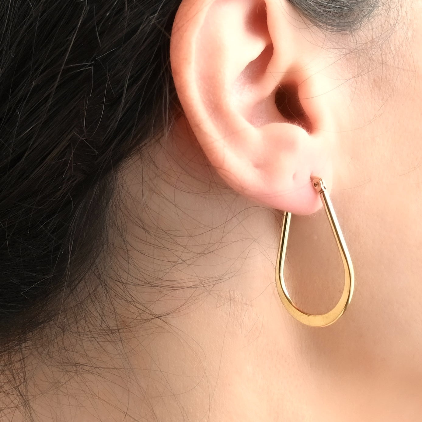 Close-up view of dainty gold waterdrop hoop earrings worn by a person with dark hair.