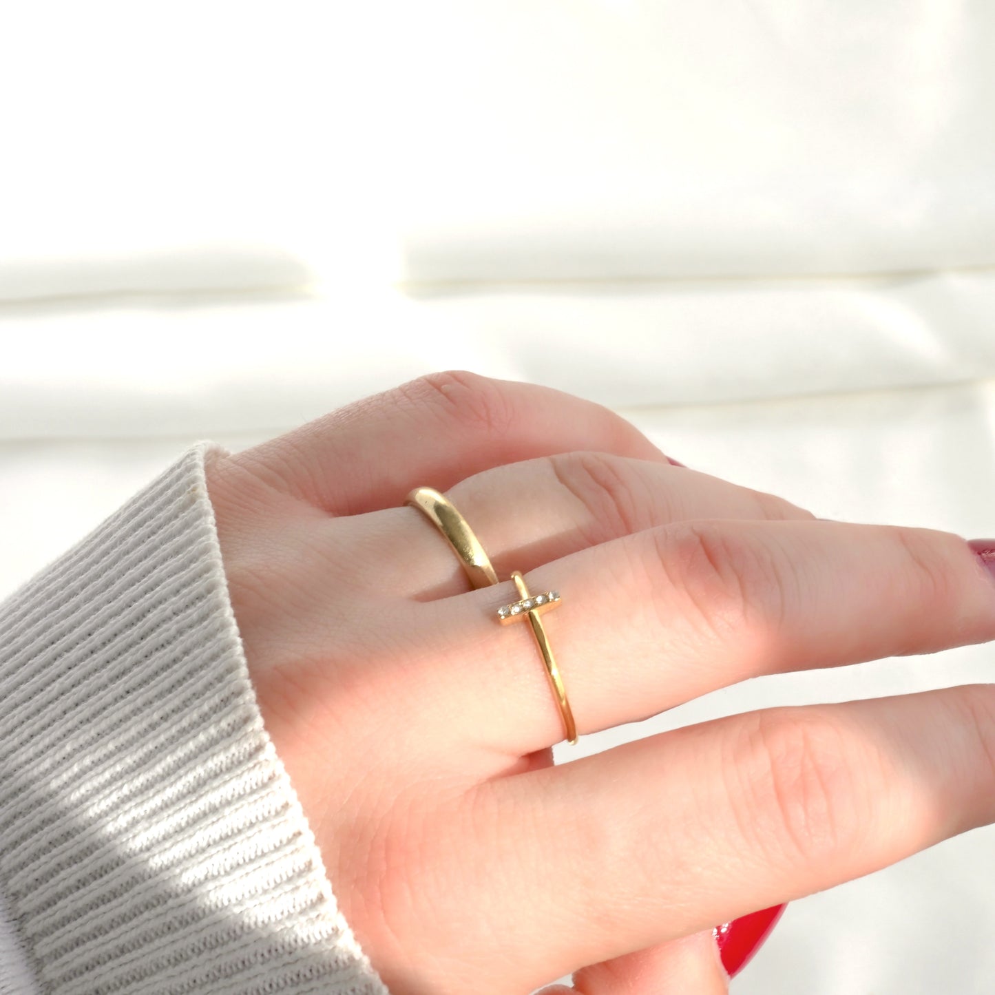 Hand wearing a gold ring with a pave CZ bar on a light background