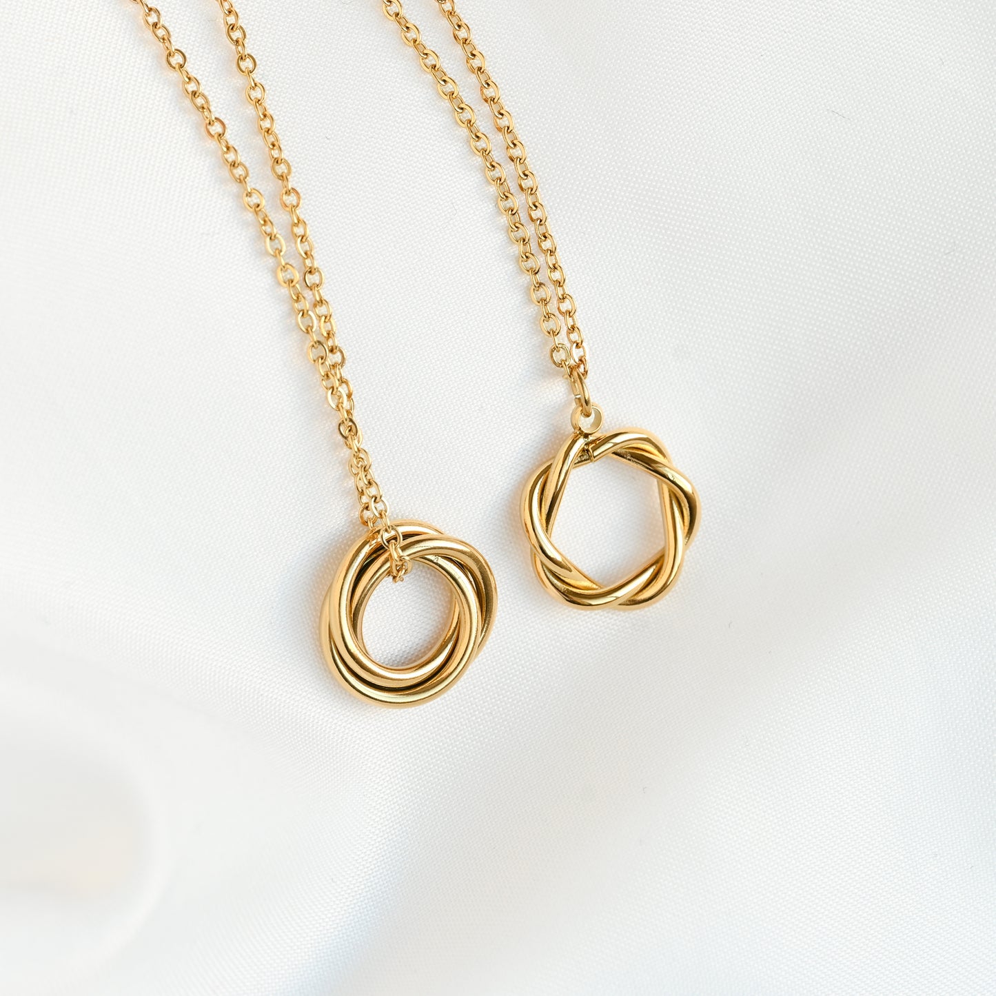 Wide angle view of two gold necklace with twisted circle pendants on a white background