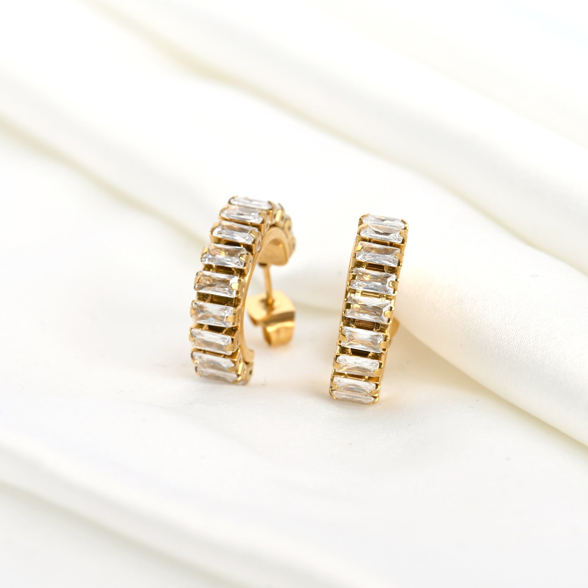 Gold diamond earrings with clear gemstones and push back closure on a white background