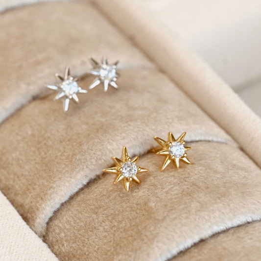 Gold and silver star-shaped earrings on a beige fabric surface
