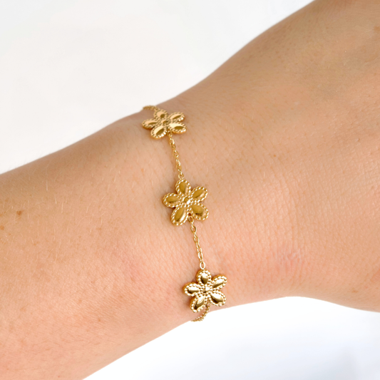 A delicate gold chain bracelet with three textured flower charms, shown worn on a person's wrist against a clean white background.