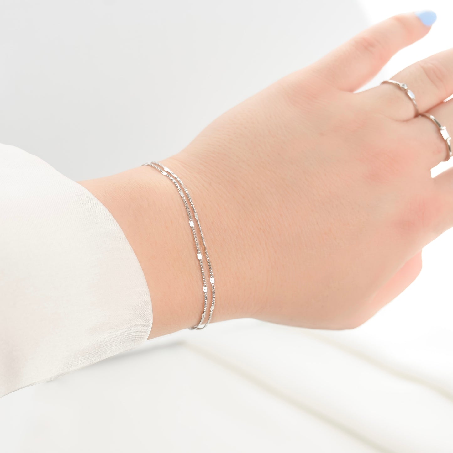 Hand wearing a silver bracelet on a plain background