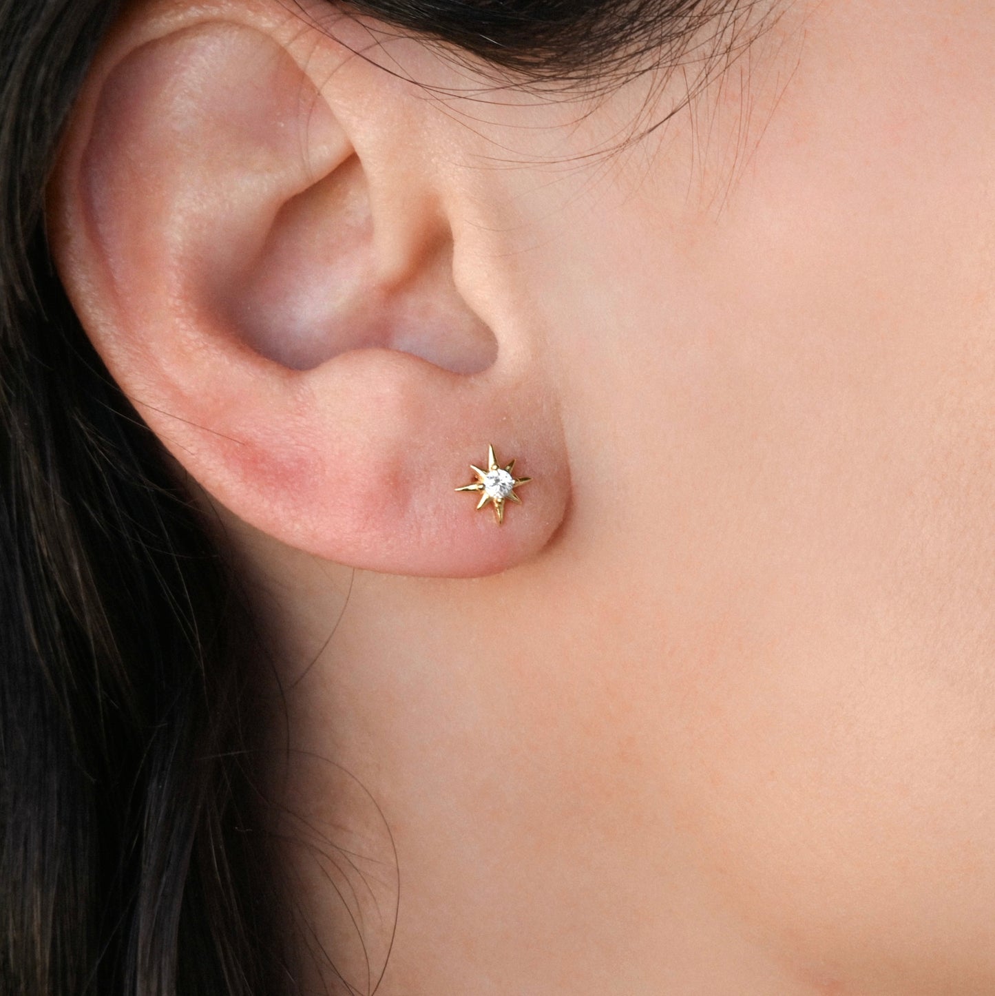 Close-up of an ear wearing a gold star-earring with a clear CZ centerpiece.