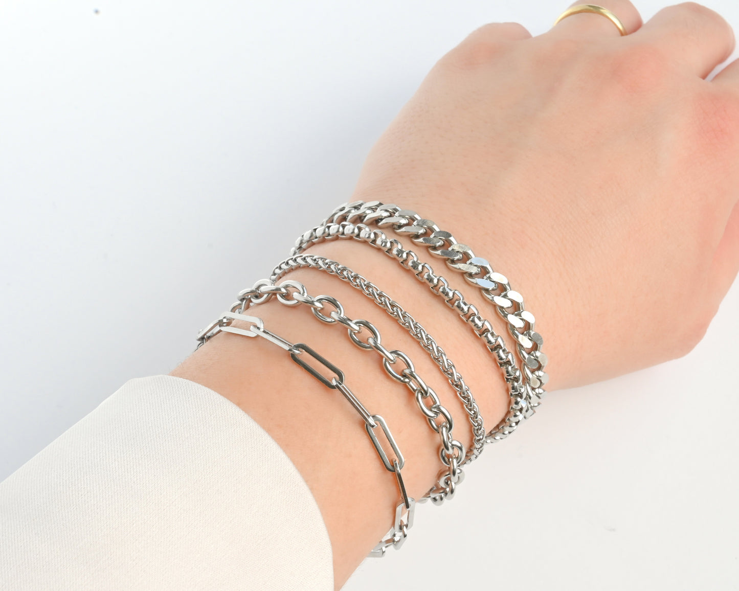 Hand wearing multiple silver bracelets on a white background