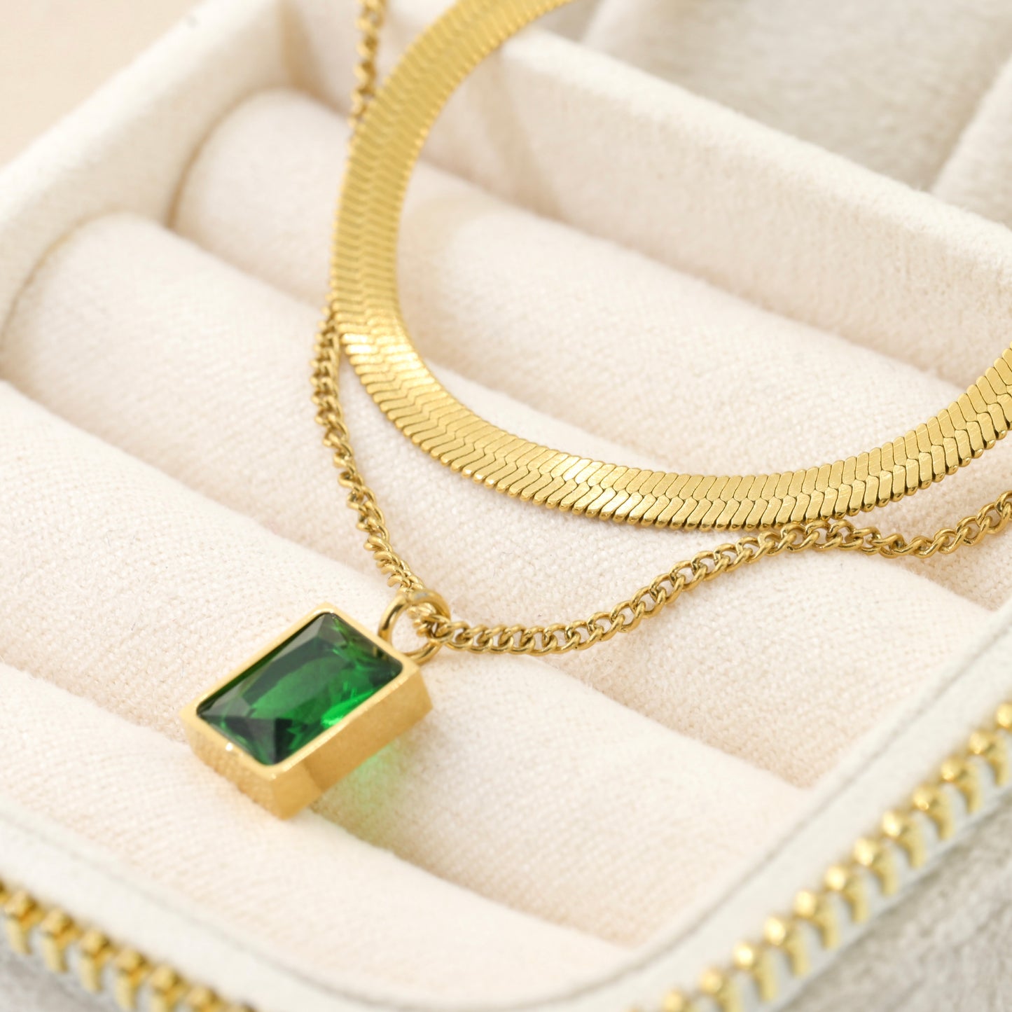 Gold necklace with a green gemstone pendant on a white cushioned surface